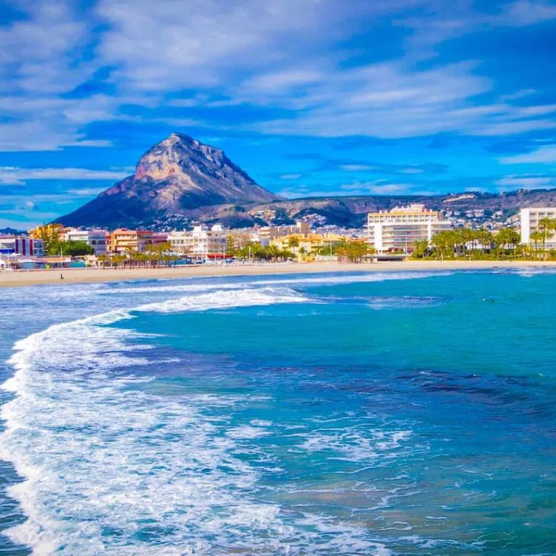 Vista panorámica de la playa de Jávea con el Montgó al fondo. Edificios residenciales bordean la costa.
