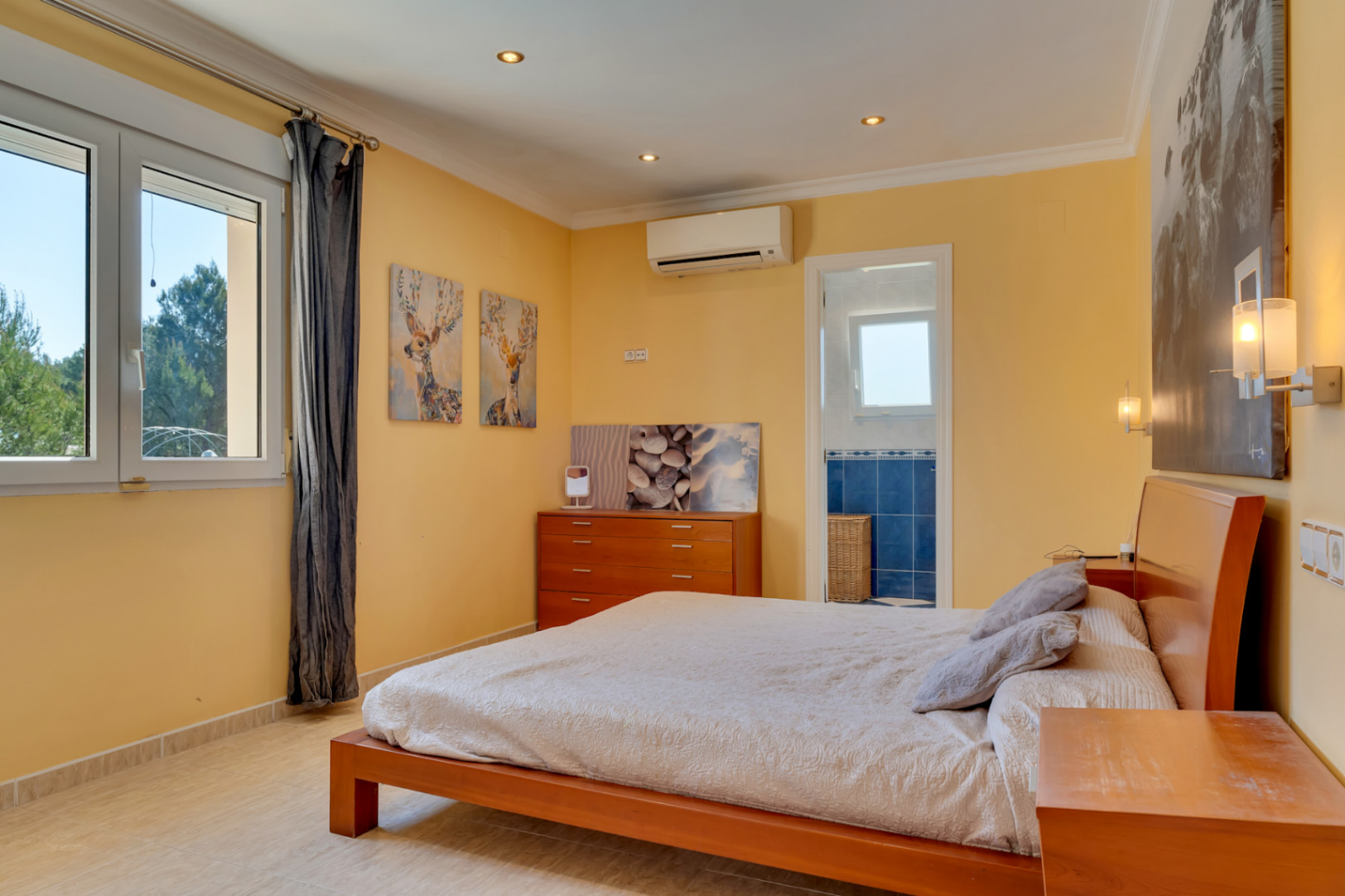 Dormitorio luminoso con aire acondicionado, suelos de gres y acceso directo a baño privado. Cuenta con ventanales de PVC que ofrecen vistas despejadas a la naturaleza circundante.