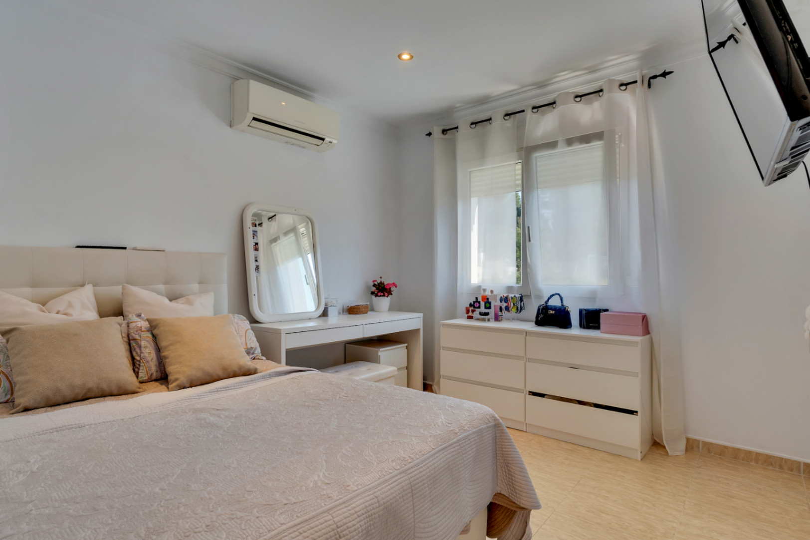 Dormitorio luminoso con cama de matrimonio, tocador blanco y cómoda a juego. Incluye aire acondicionado split, suelos cerámicos y televisión de pared.