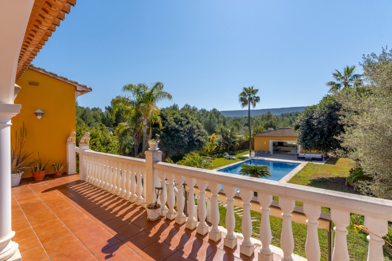 Terraza superior con suelo de terracota y balaustrada blanca, ofreciendo vistas despejadas a la piscina de 15x6m, el jardín mediterráneo y el entorno natural protegido.