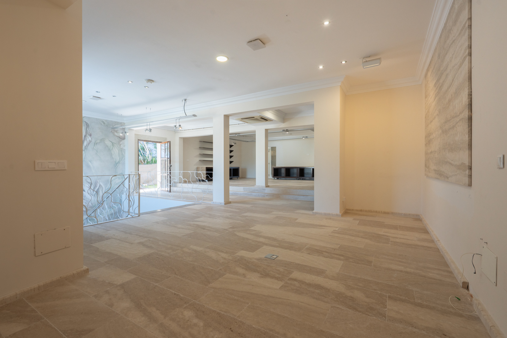 Amplia zona de recepción con suelos de piedra natural, iluminación empotrada y una escalera con barandilla decorativa que conecta los niveles comerciales.