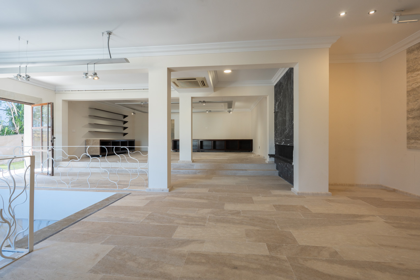 Amplio espacio diáfano con suelos de piedra natural, pilares estructurales, iluminación empotrada y una pared decorativa de mármol negro.
