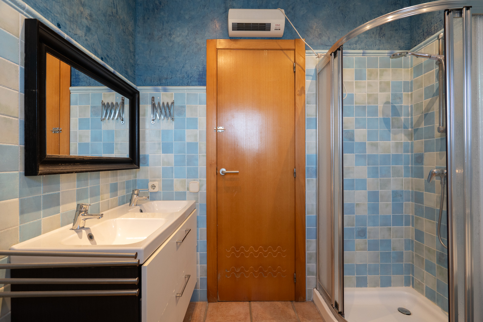 Baño equipado con lavabo doble, ducha de esquina con mampara curva y paredes revestidas con azulejos en diversos tonos azules.