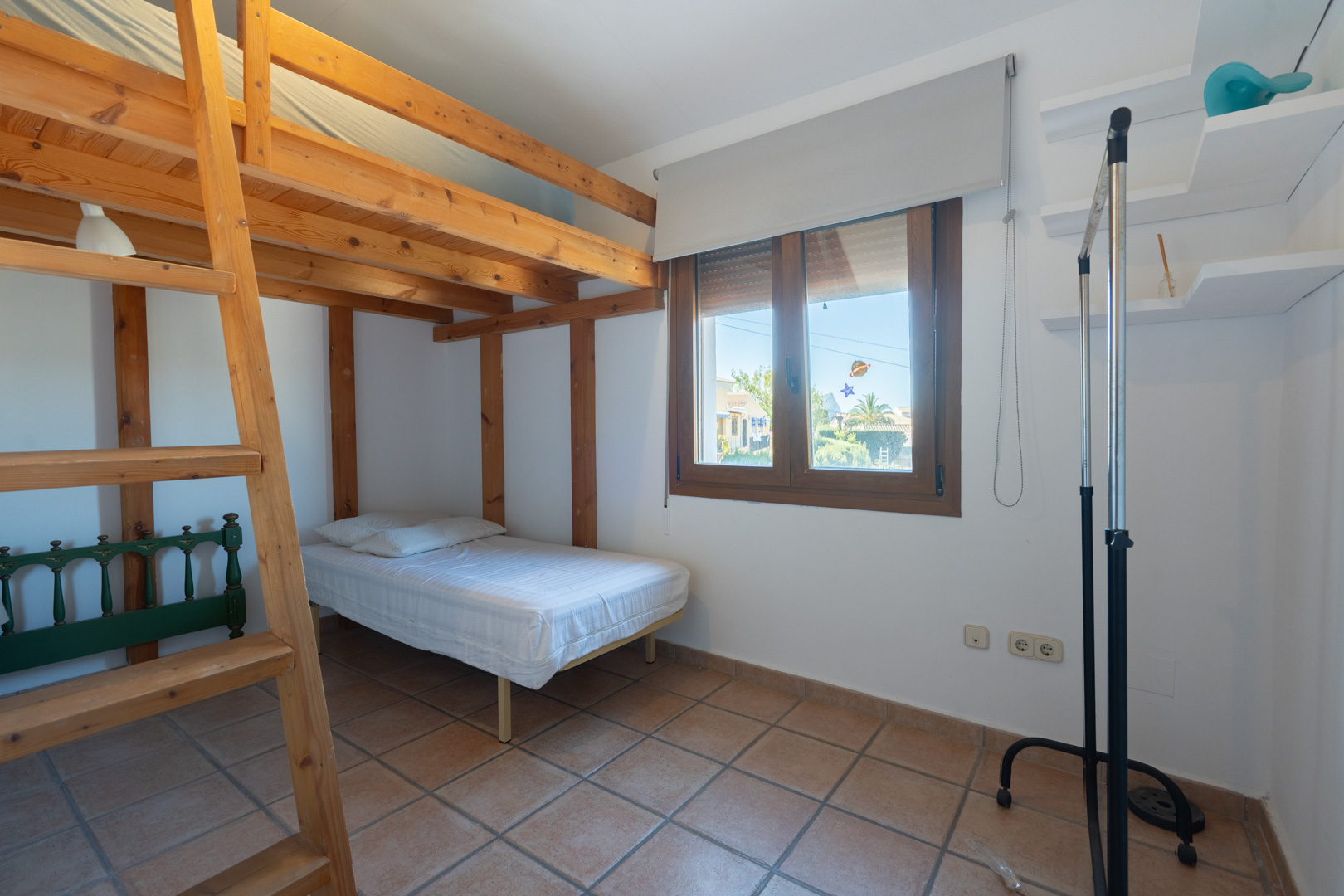 Dormitorio con estructura de litera en madera maciza, suelos de gres rústico y ventana con marco de madera que aporta luz natural.