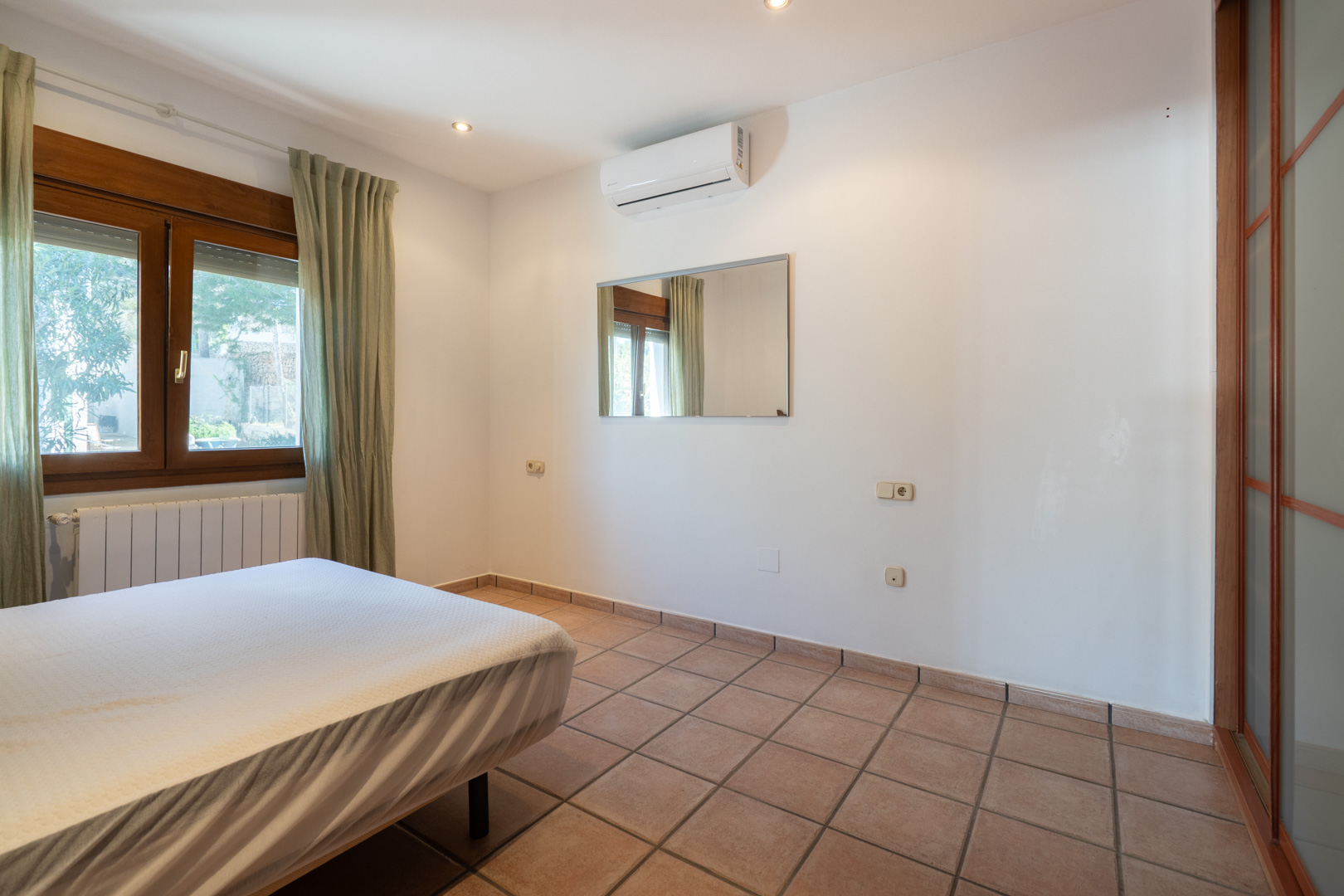Dormitorio con suelos de gres, aire acondicionado split y ventana de madera. Incluye iluminación empotrada y un armario con puertas correderas.