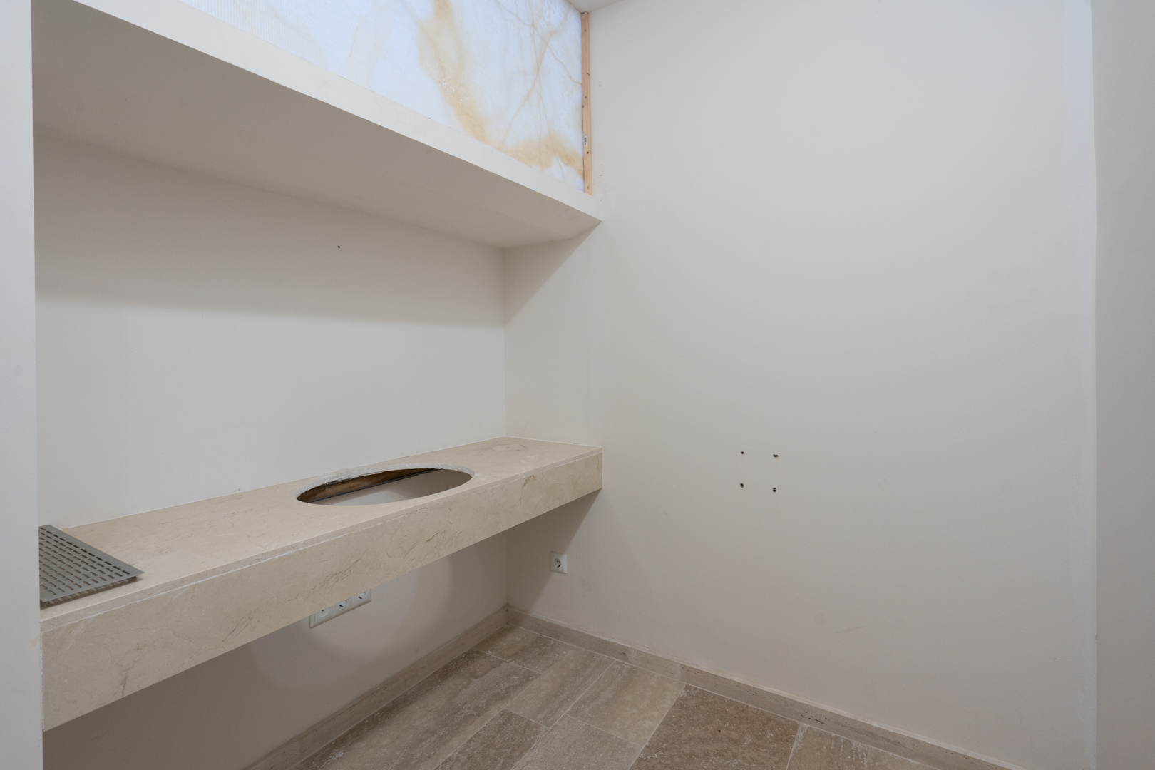 Encimera de piedra natural con hueco para lavabo encastrado, estante superior a juego y suelos de gres en tonos neutros.