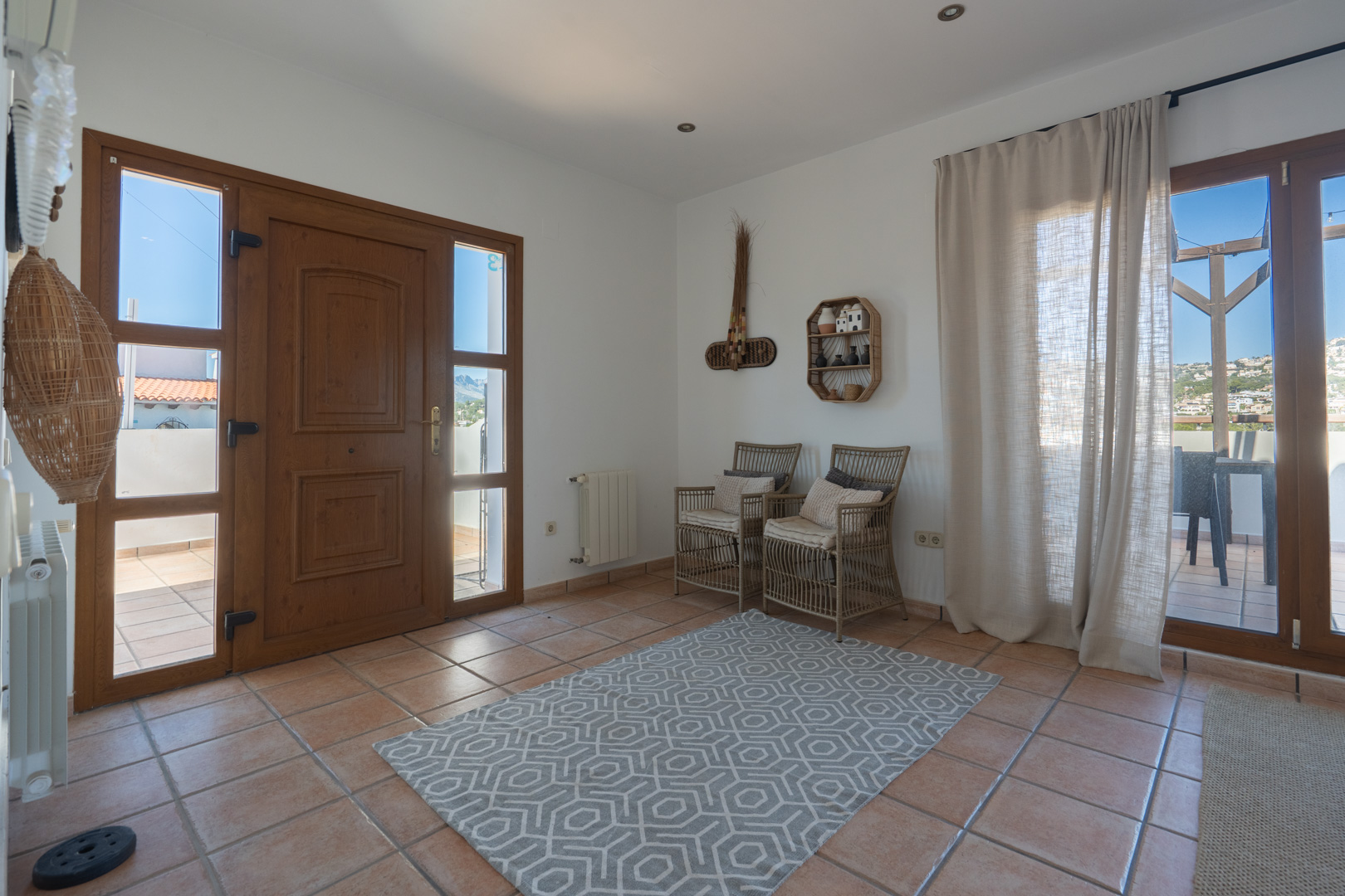 Entrada a la vivienda con suelos de terracota, puerta de madera con paneles laterales de cristal y acceso directo a la terraza exterior mediante puertas acristaladas.