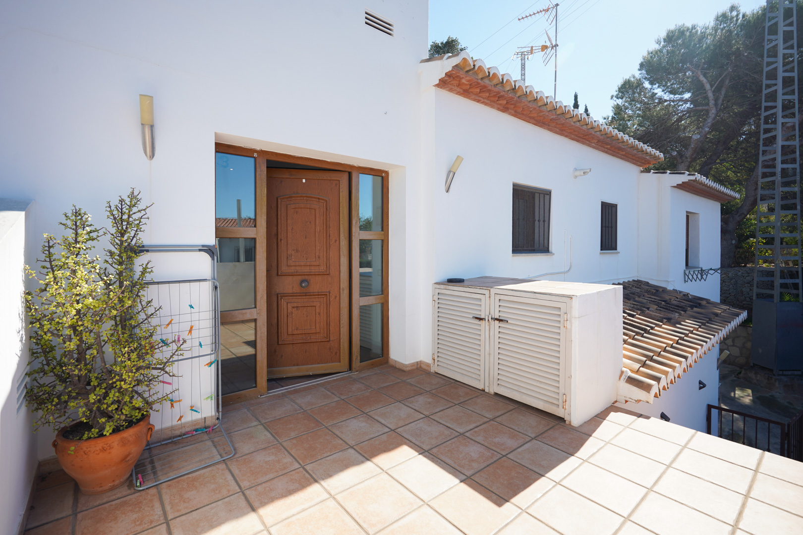 Entrada independiente a la planta superior con terraza de baldosas cerámicas, puerta de madera con paneles de cristal y muros blancos tradicionales.