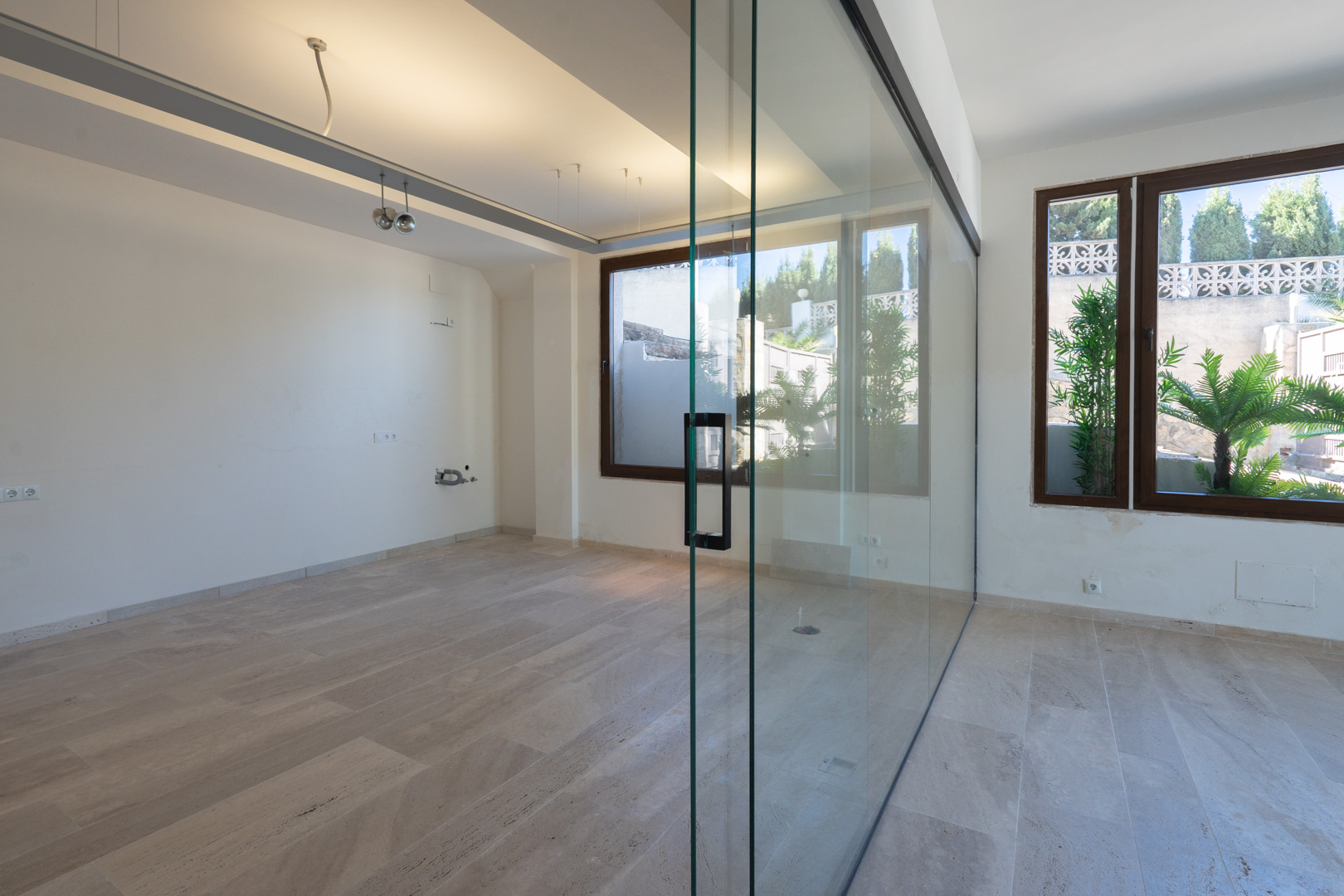 Espacio comercial diáfano con suelos de piedra natural, paredes blancas y una gran mampara de cristal divisoria que permite la entrada de luz natural.
