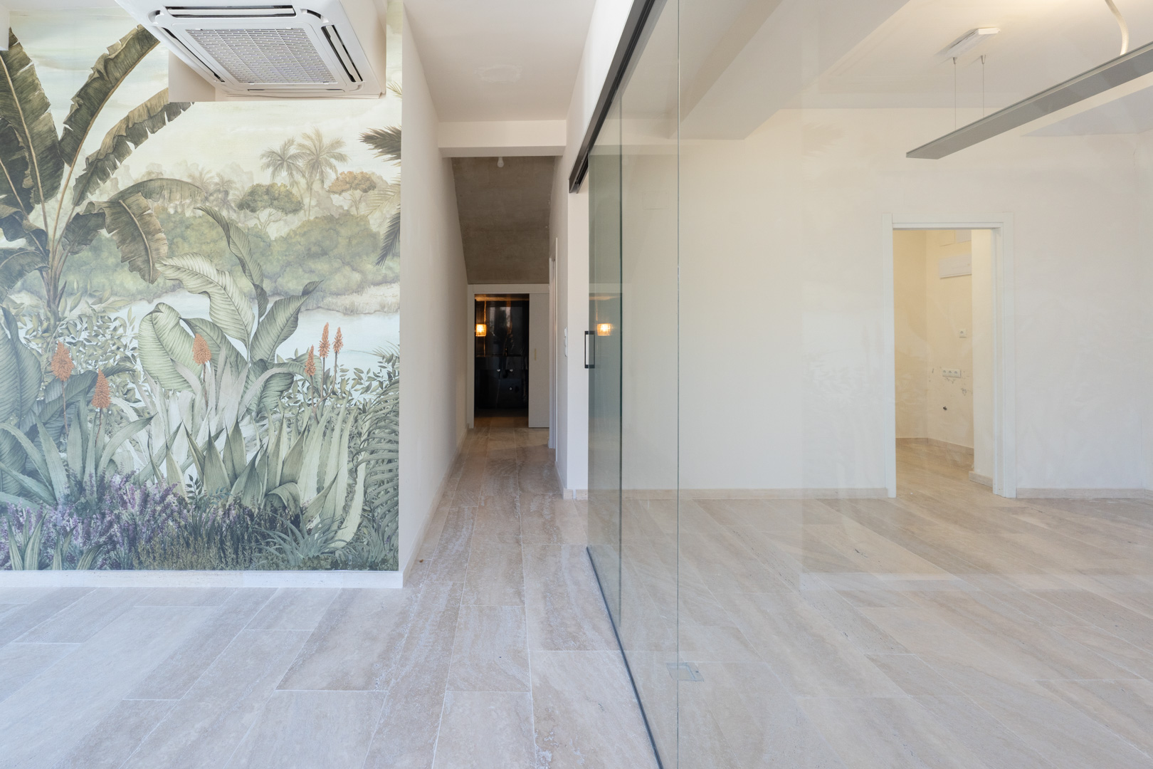 Espacio comercial luminoso con suelos de gres porcelánico, tabique de cristal y un mural decorativo tropical. Incluye climatización por casete en el techo.