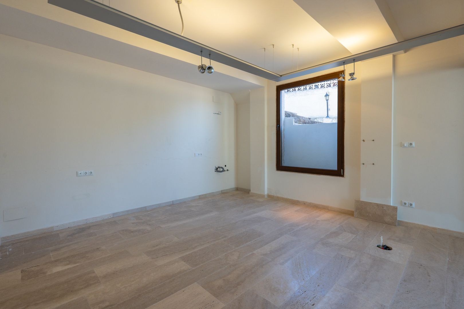 Espacio interior diáfano con suelos de piedra natural, iluminación técnica empotrada y ventanal con marco de madera. Incluye preinstalaciones eléctricas y de fontanería.