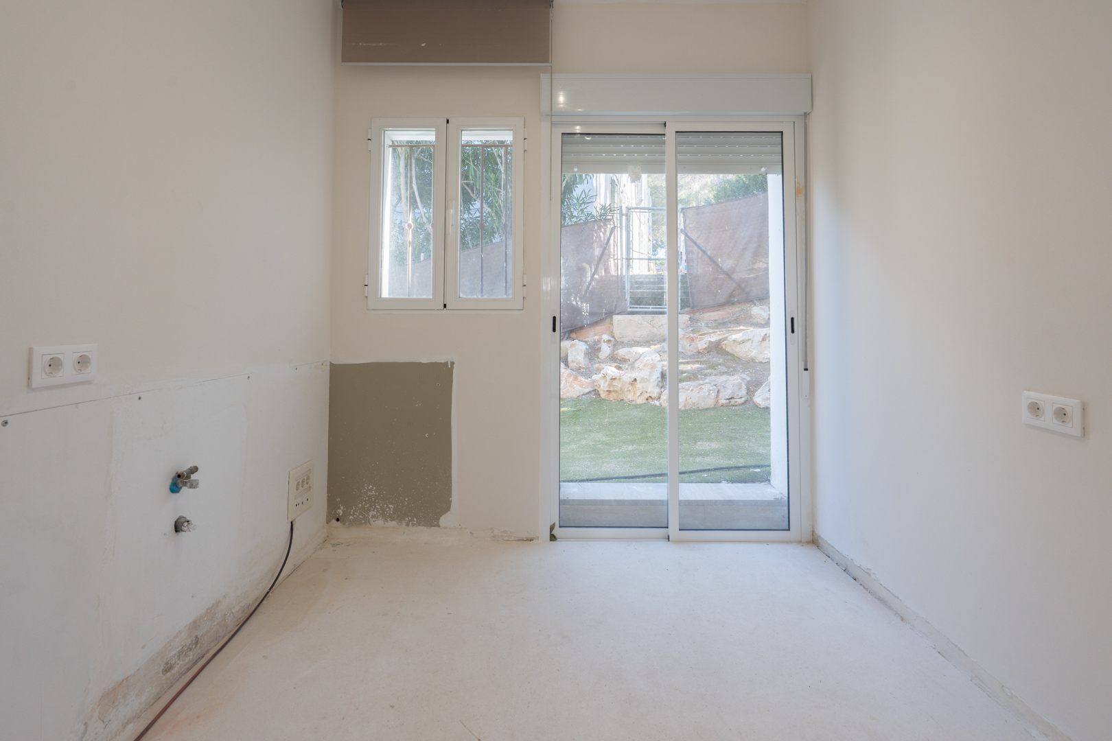 Estancia diáfana con preinstalación de fontanería, carpintería exterior de aluminio blanco y acceso directo al jardín mediante puerta corredera.