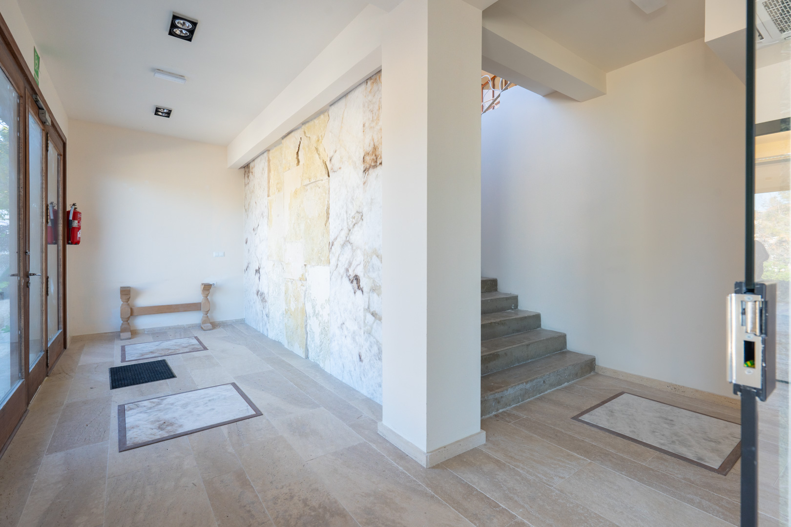 Hall de entrada con pared decorativa de piedra natural, suelos de gres con incrustaciones de mármol y acceso a la planta superior mediante escalera.