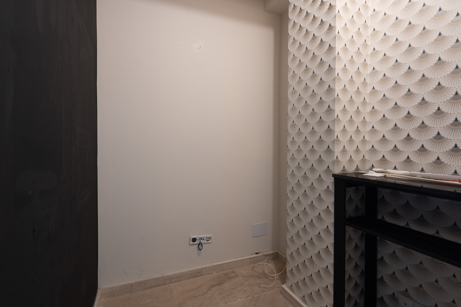 Rincón interior con papel pintado de patrón Art Déco, suelos de piedra natural y tomas eléctricas integradas en una de las estancias comerciales.