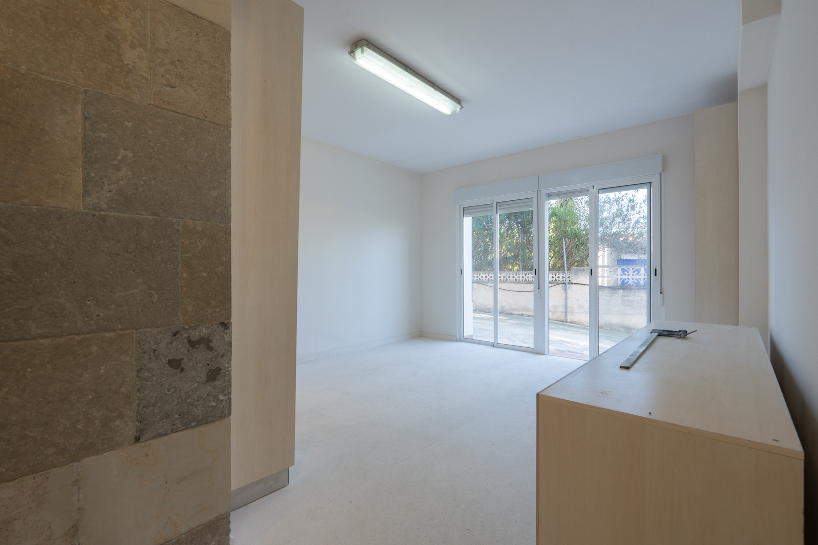 Sala comercial diáfana con pared decorativa de piedra natural, iluminación fluorescente y acceso directo al exterior mediante puertas correderas de cristal.