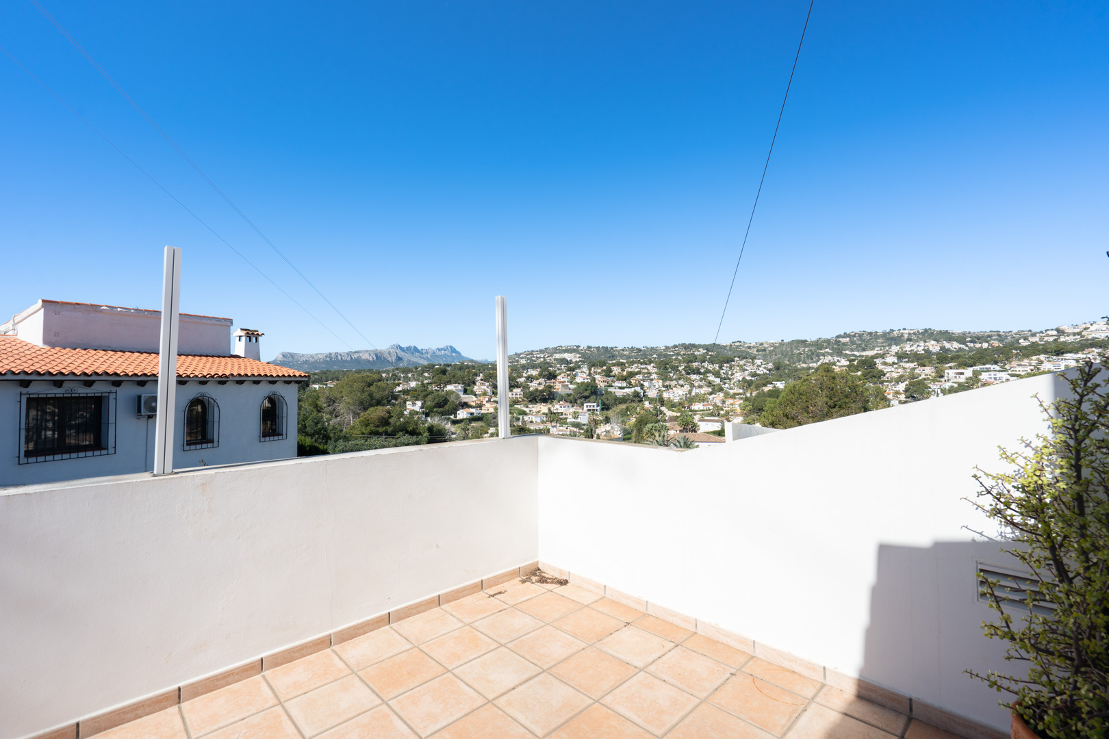 Terraza exterior con suelo de baldosas cerámicas y muros blancos, ofreciendo vistas despejadas a la Sierra de Bernia y al entorno residencial arbolado.