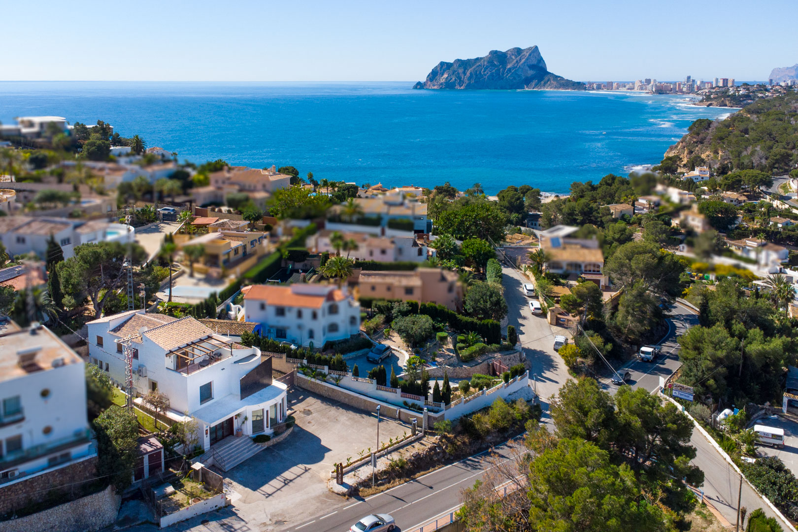 Vista aérea de la propiedad de tres plantas con amplio aparcamiento privado, situada junto a la carretera costera con vistas panorámicas al mar y al Peñón de Ifach.