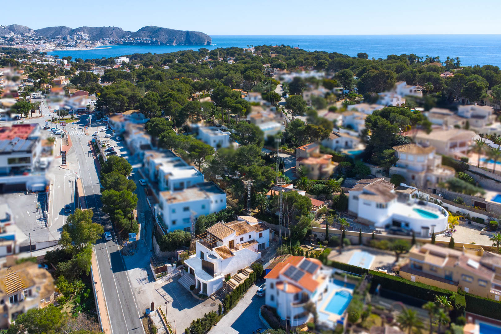 Vista aérea de la propiedad junto a la carretera Moraira-Calpe, mostrando su estructura blanca de tres niveles, aparcamiento privado y vistas al litoral mediterráneo.