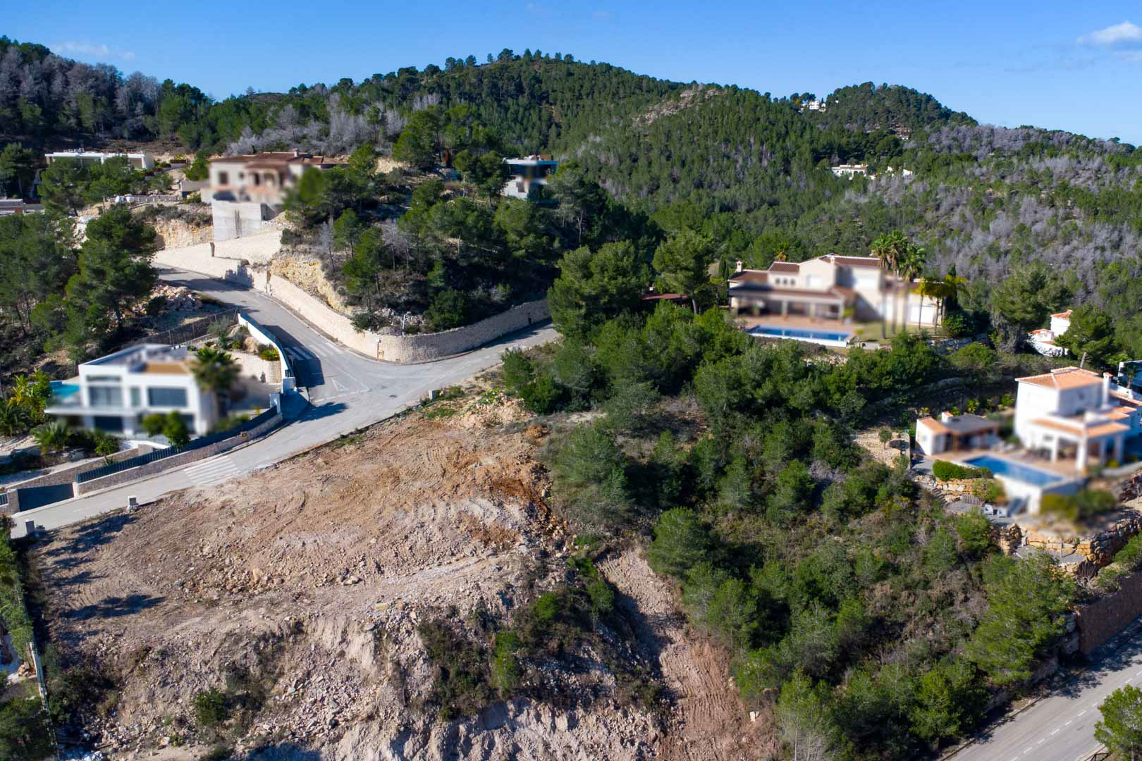 Vista aérea de la parcela elevada rodeada de naturaleza, mostrando el terreno preparado para la construcción y la proximidad a villas vecinas con piscina.