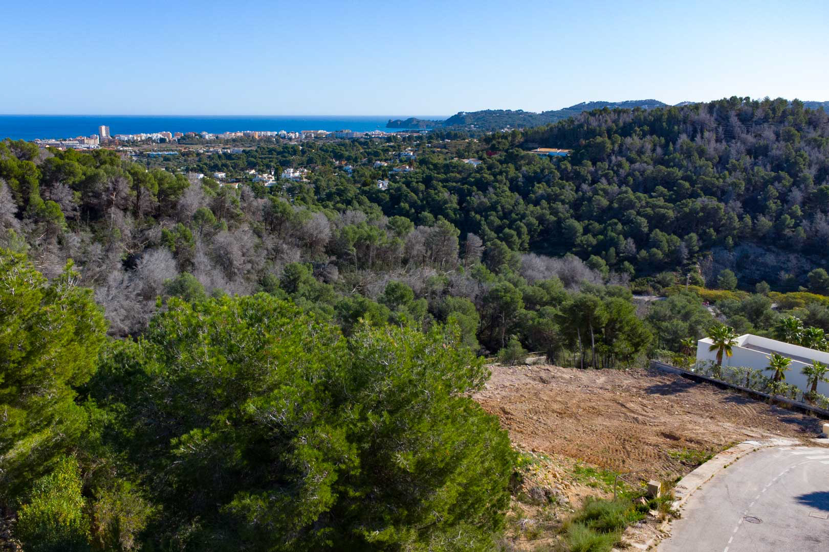 Vistas panorámicas al mar Mediterráneo y al entorno natural de pinos desde la ubicación elevada de la propiedad, con el núcleo urbano costero en el horizonte.