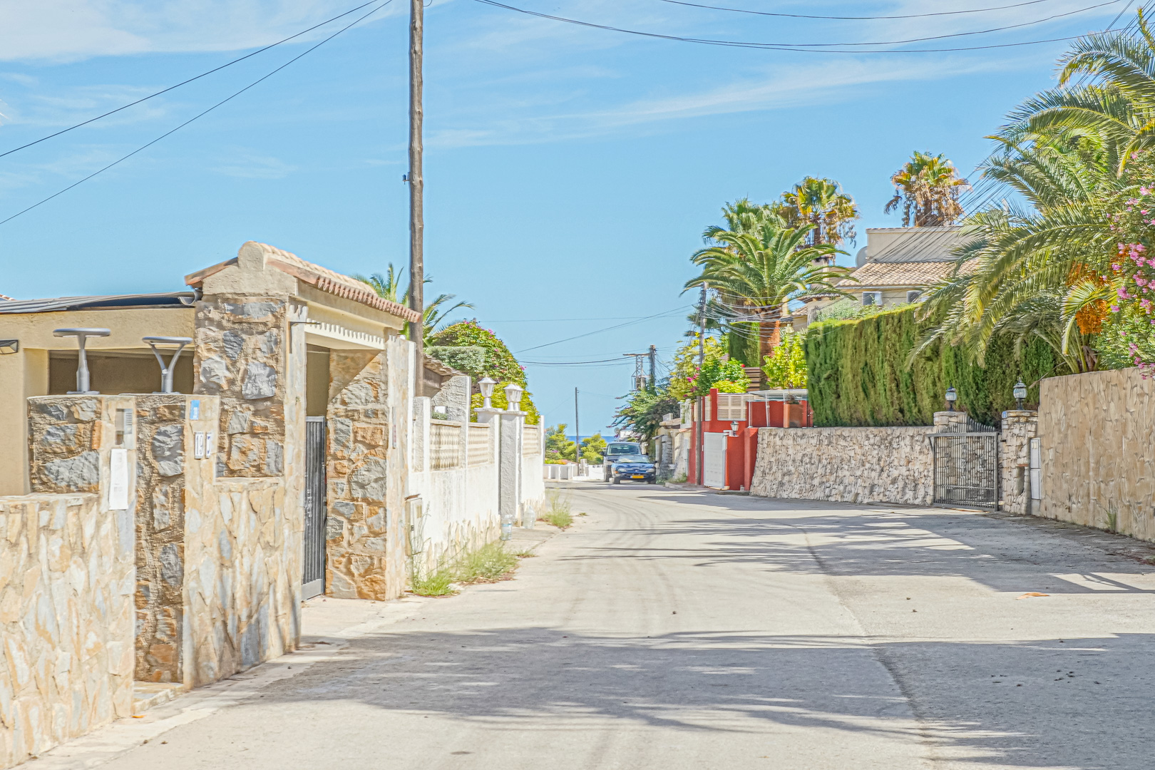 Vista de la calle residencial pavimentada con muros de piedra natural y palmeras, situada a pocos metros de la costa en Benissa.