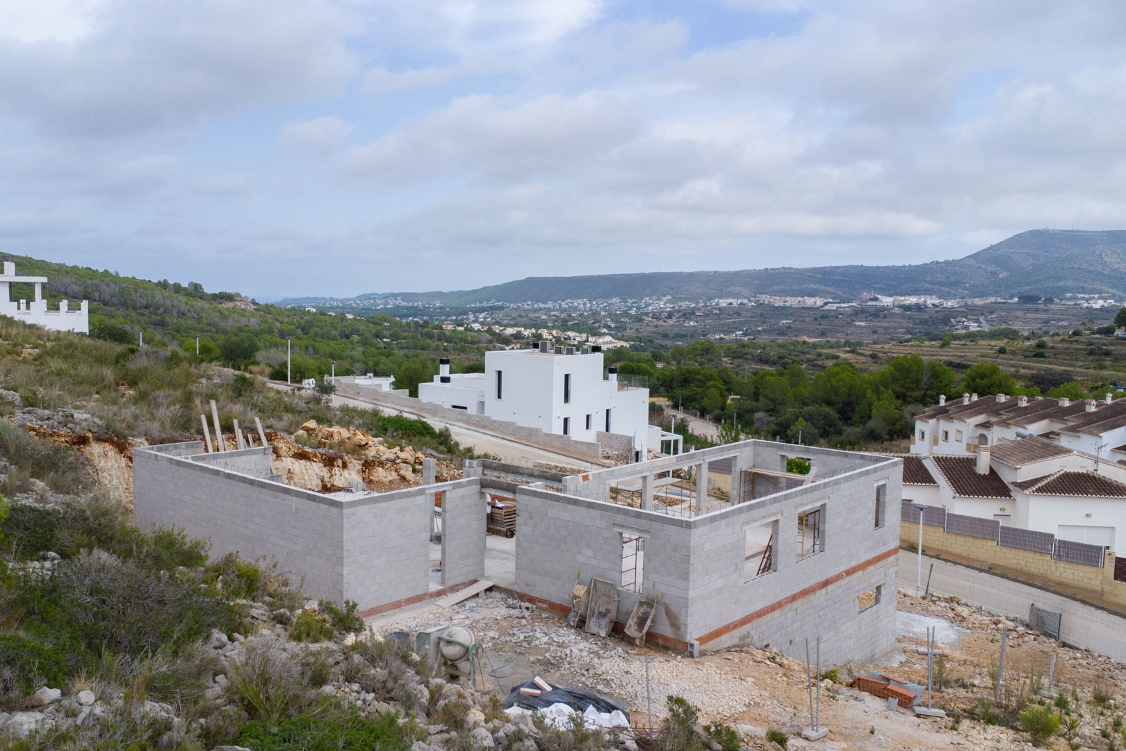 Fase de construcción de una villa moderna en Pedreguer, mostrando la estructura de bloques de hormigón y vistas panorámicas al valle y las montañas.