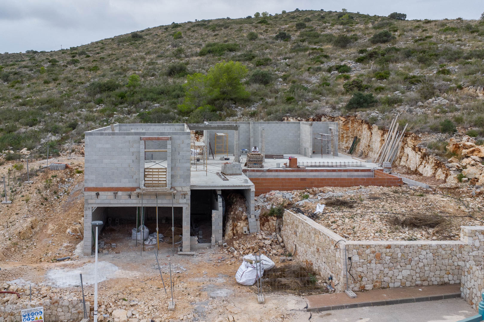 Obra en curso de una villa moderna en Pedreguer, mostrando la estructura de hormigón, muros de piedra seca y su integración en la ladera natural.
