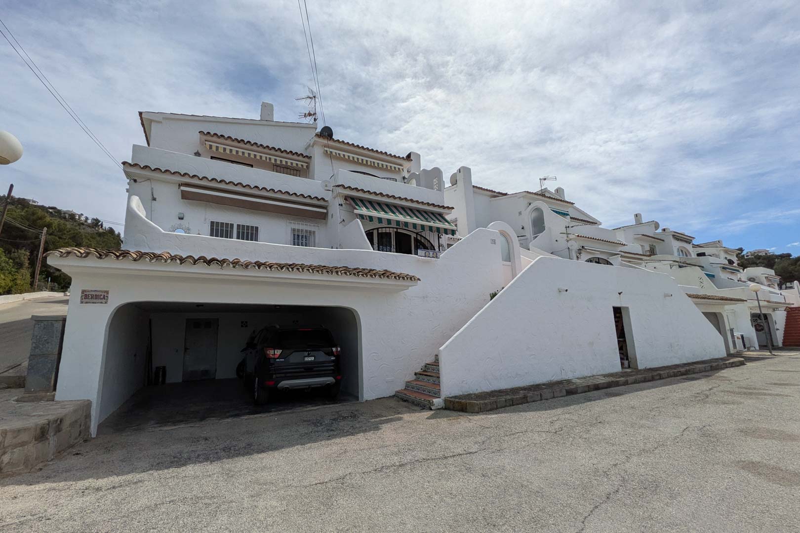 Fachada exterior con cochera privada a nivel de calle y escaleras de acceso con azulejos tradicionales que conectan los dos niveles de la vivienda.