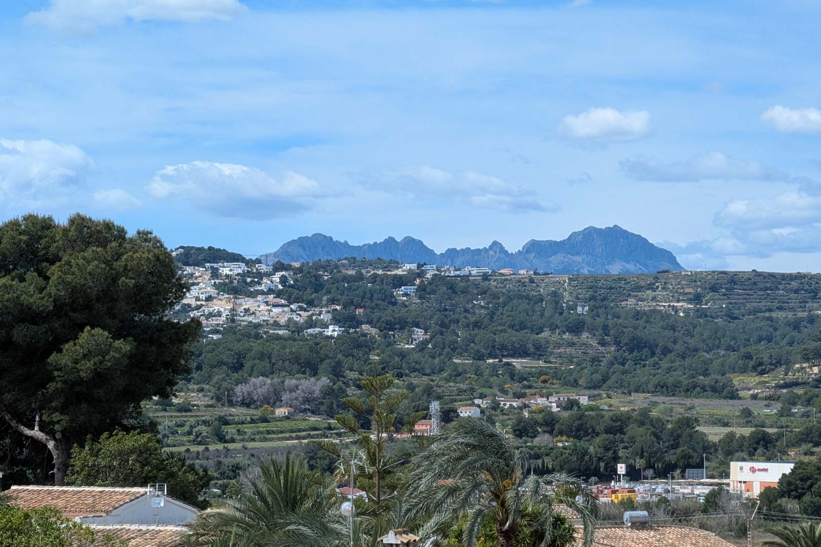 Vistas panorámicas desde la terraza hacia el valle y las montañas, mostrando la vegetación mediterránea y el entorno residencial de Moraira bajo un cielo despejado.