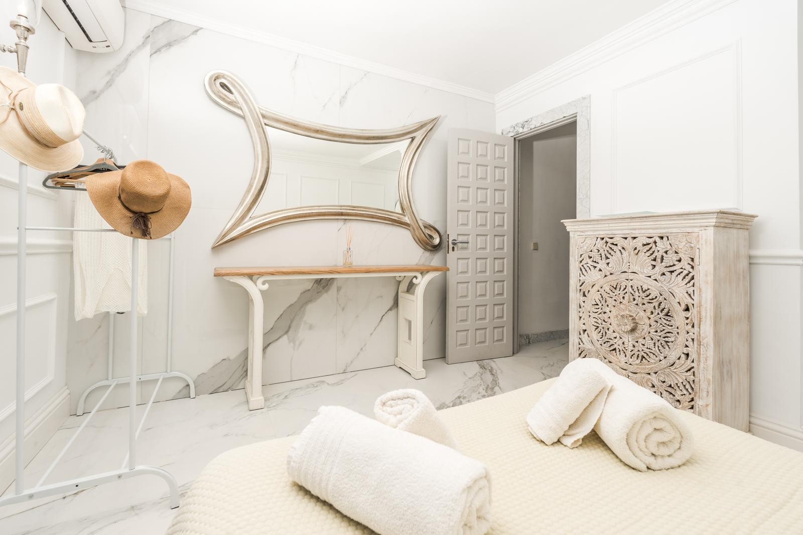 Dormitorio con paredes de mármol, espejo de diseño orgánico y cómoda de madera tallada. Incluye suelos de gres porcelánico y aire acondicionado de alta eficiencia.