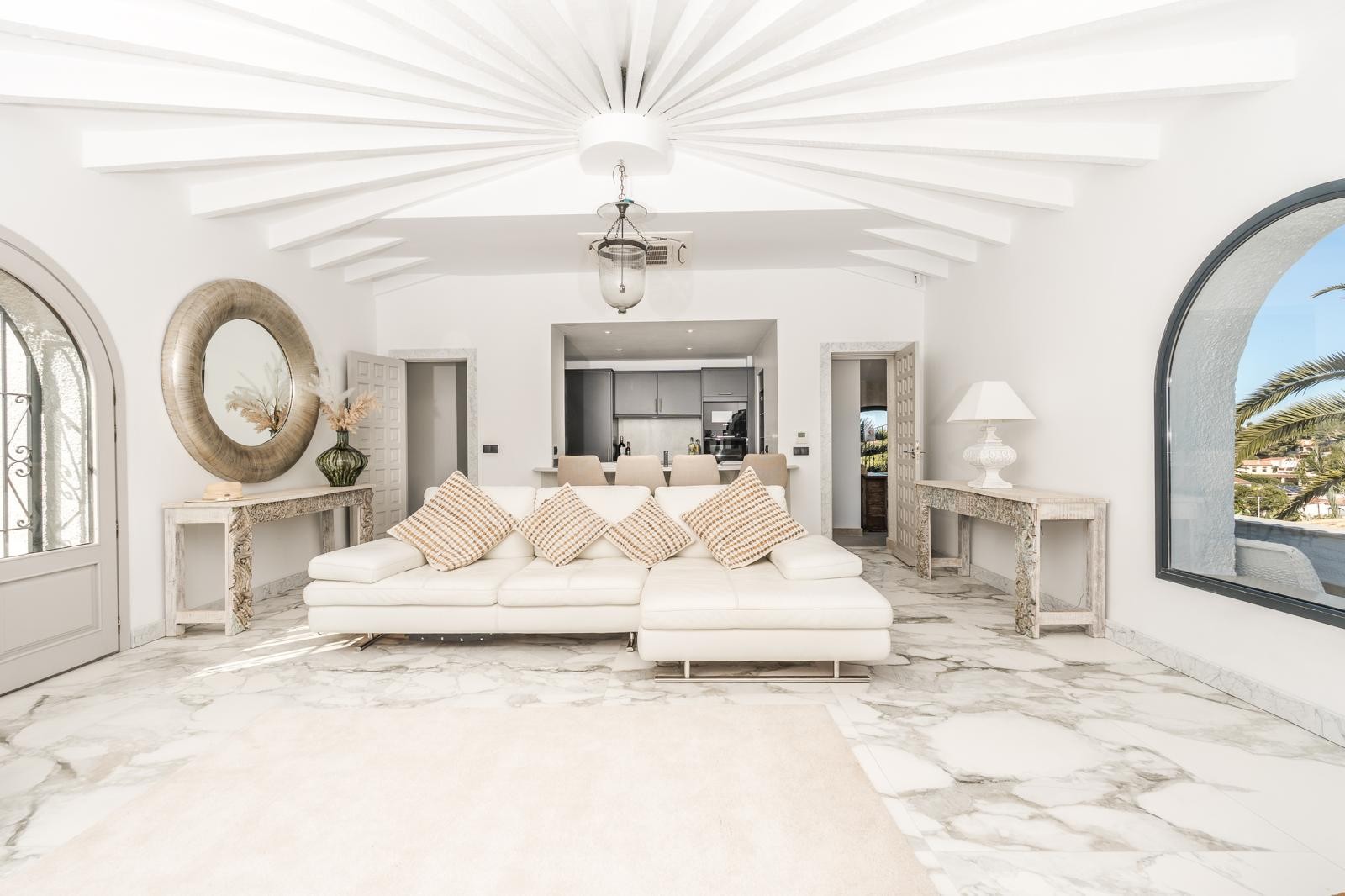 Salón de diseño circular con techos de vigas radiales blancas, suelo de mármol veteado y grandes ventanales en arco que ofrecen vistas al entorno mediterráneo.