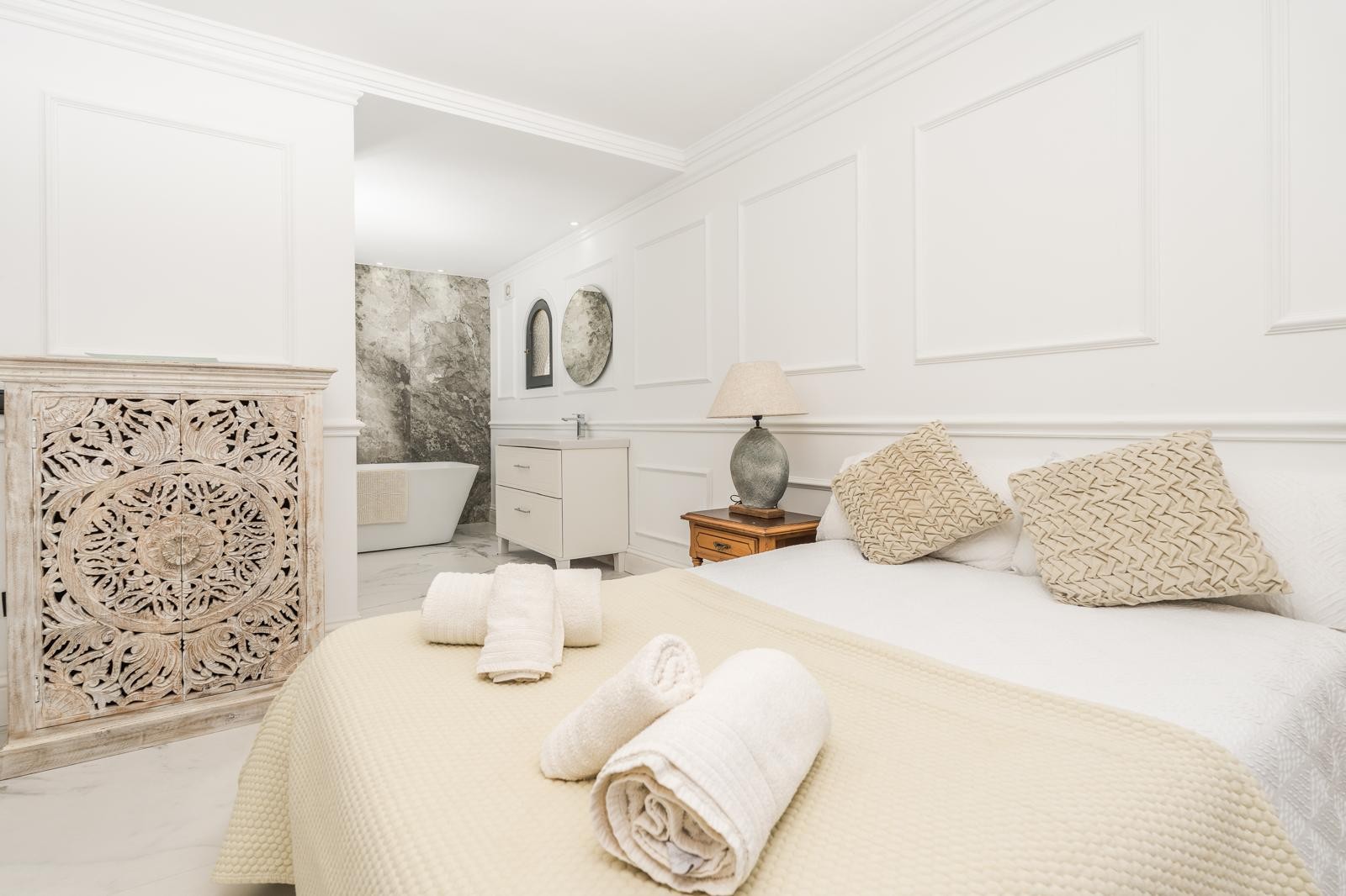 Suite principal con molduras decorativas, armario de madera tallada y baño integrado con bañera exenta y revestimientos de mármol.