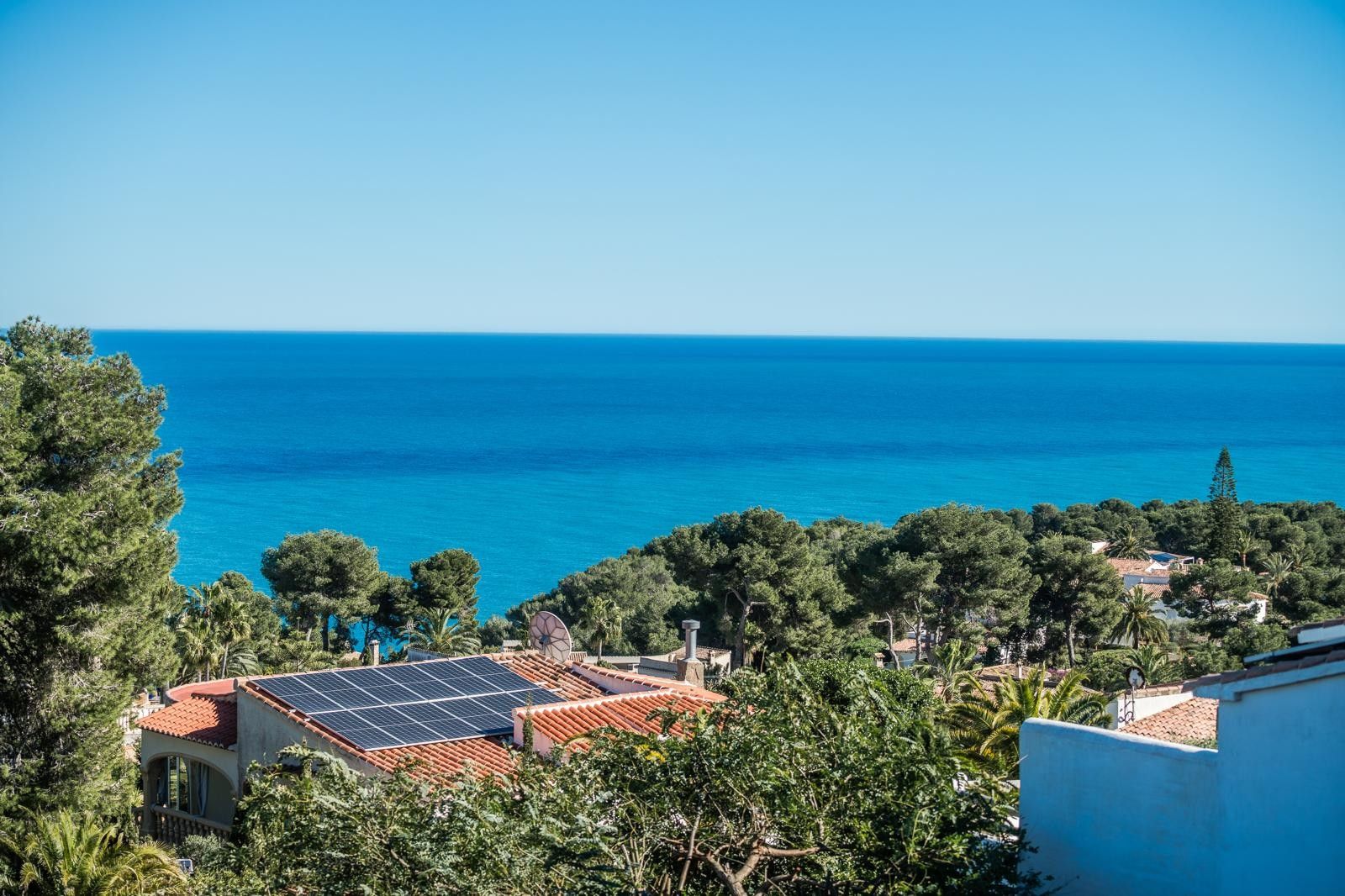 Vistas panorámicas al mar Mediterráneo desde Balcón al Mar, destacando el entorno de pinos y tejados con paneles solares bajo un cielo despejado.