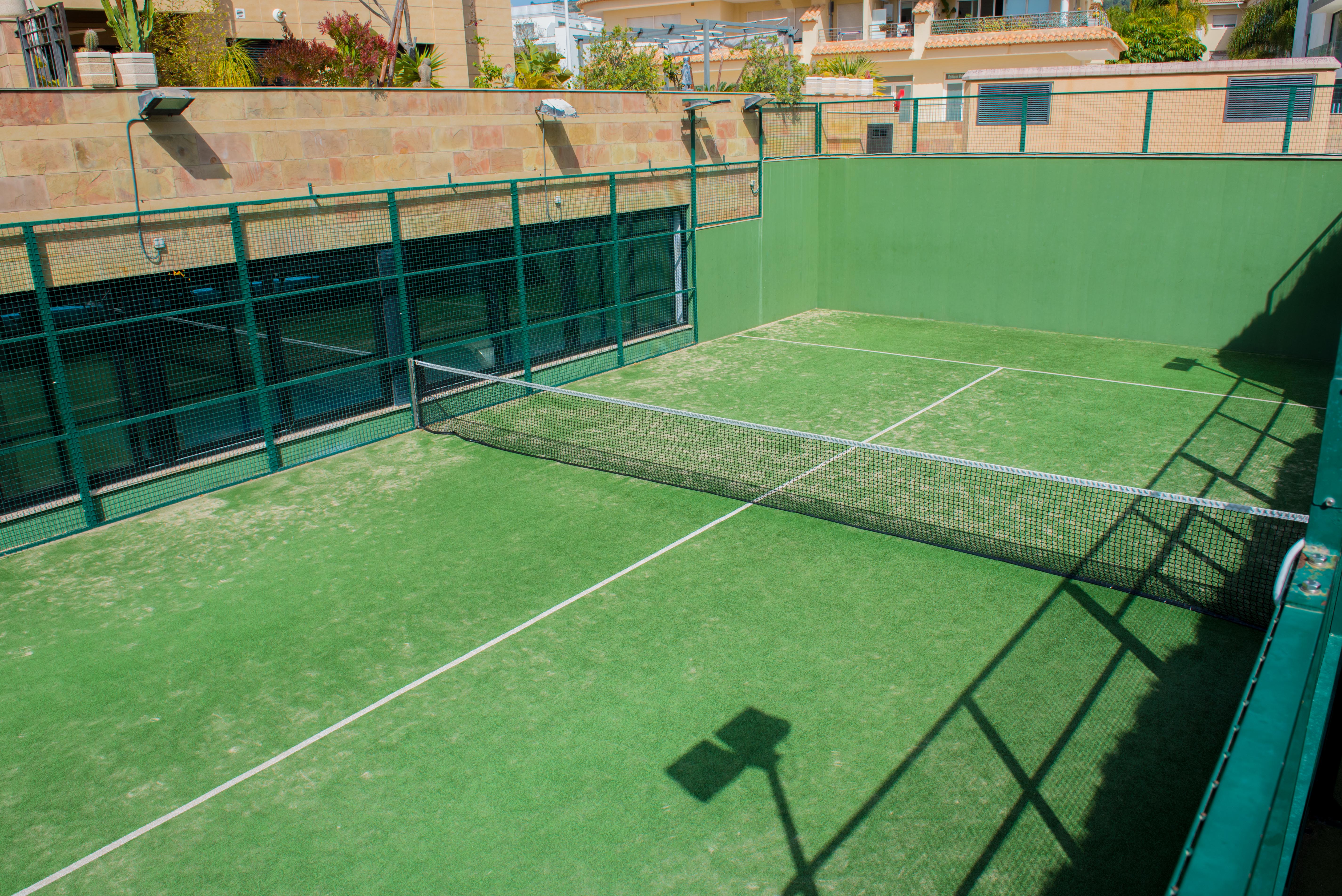 Pista de pádel privada con césped artificial verde y cerramiento perimetral metálico, integrada en las zonas comunes del complejo residencial en Jávea.