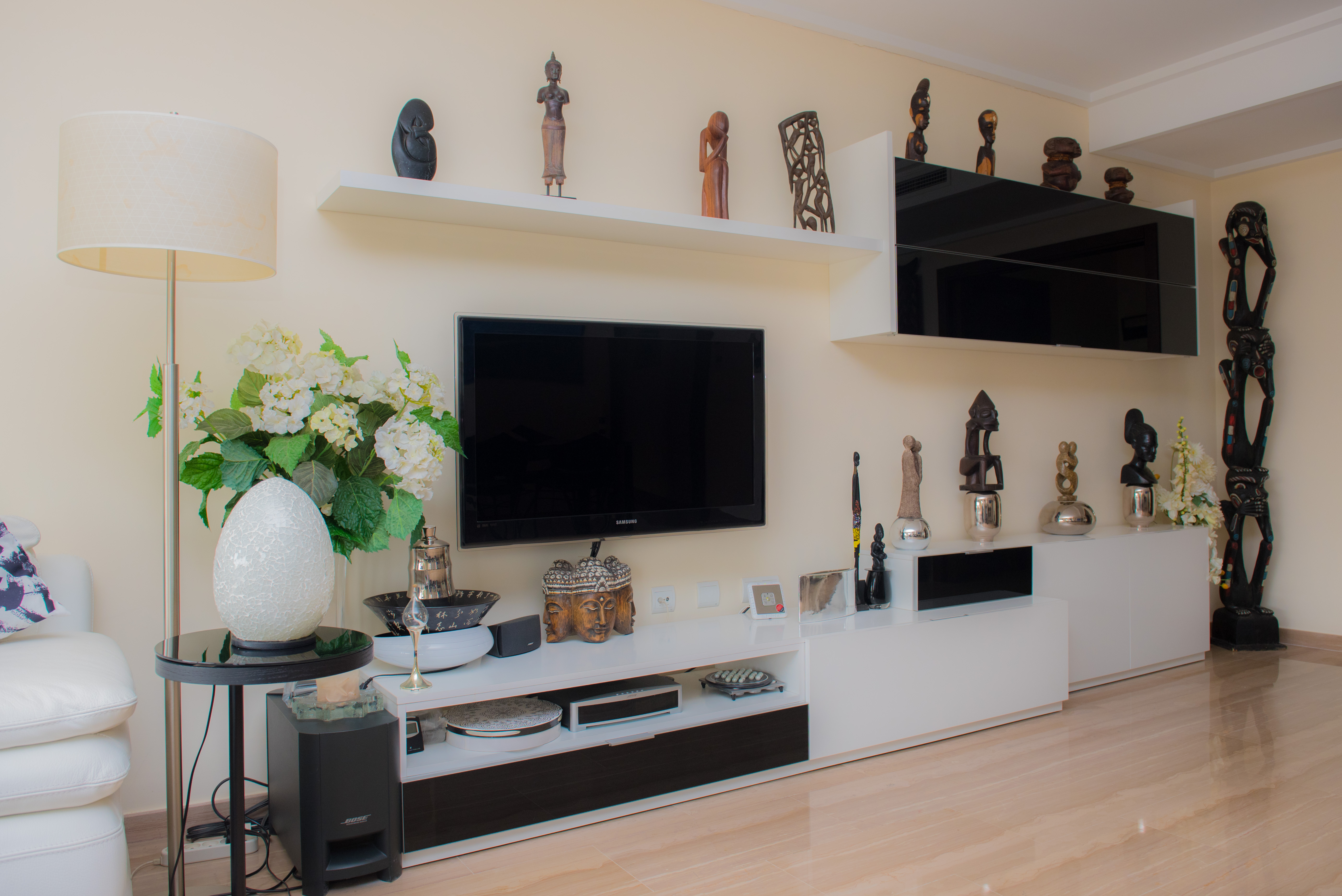 Salón con mueble de televisión minimalista en blanco y negro, estanterías flotantes decoradas con arte étnico y suelos de mármol pulido.