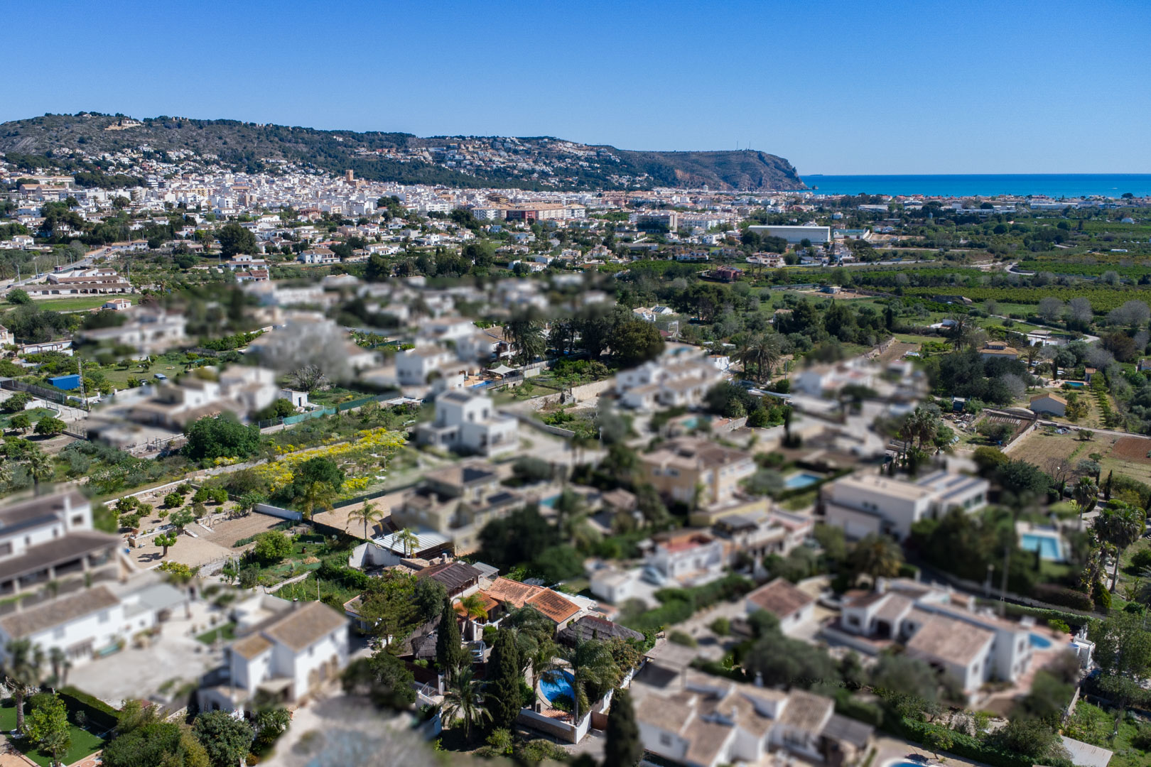 Vista aérea de la zona residencial en Jávea, mostrando la proximidad al centro urbano, la costa mediterránea y el relieve montañoso bajo un cielo despejado.