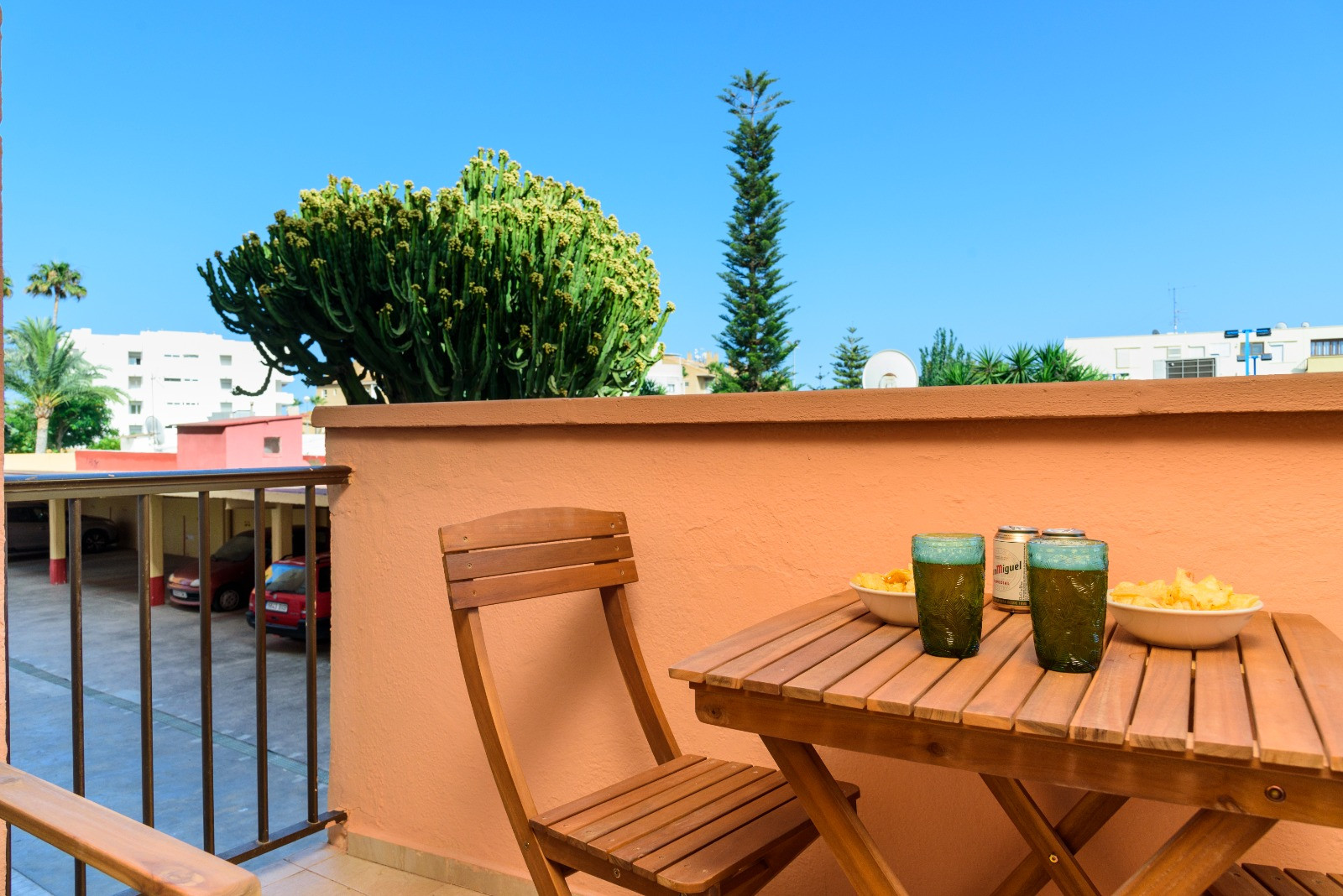 Terraza privada equipada con mobiliario de madera, ideal para aperitivos al aire libre. Ofrece vistas despejadas a zonas ajardinadas con cactus y palmeras bajo un cielo despejado.
