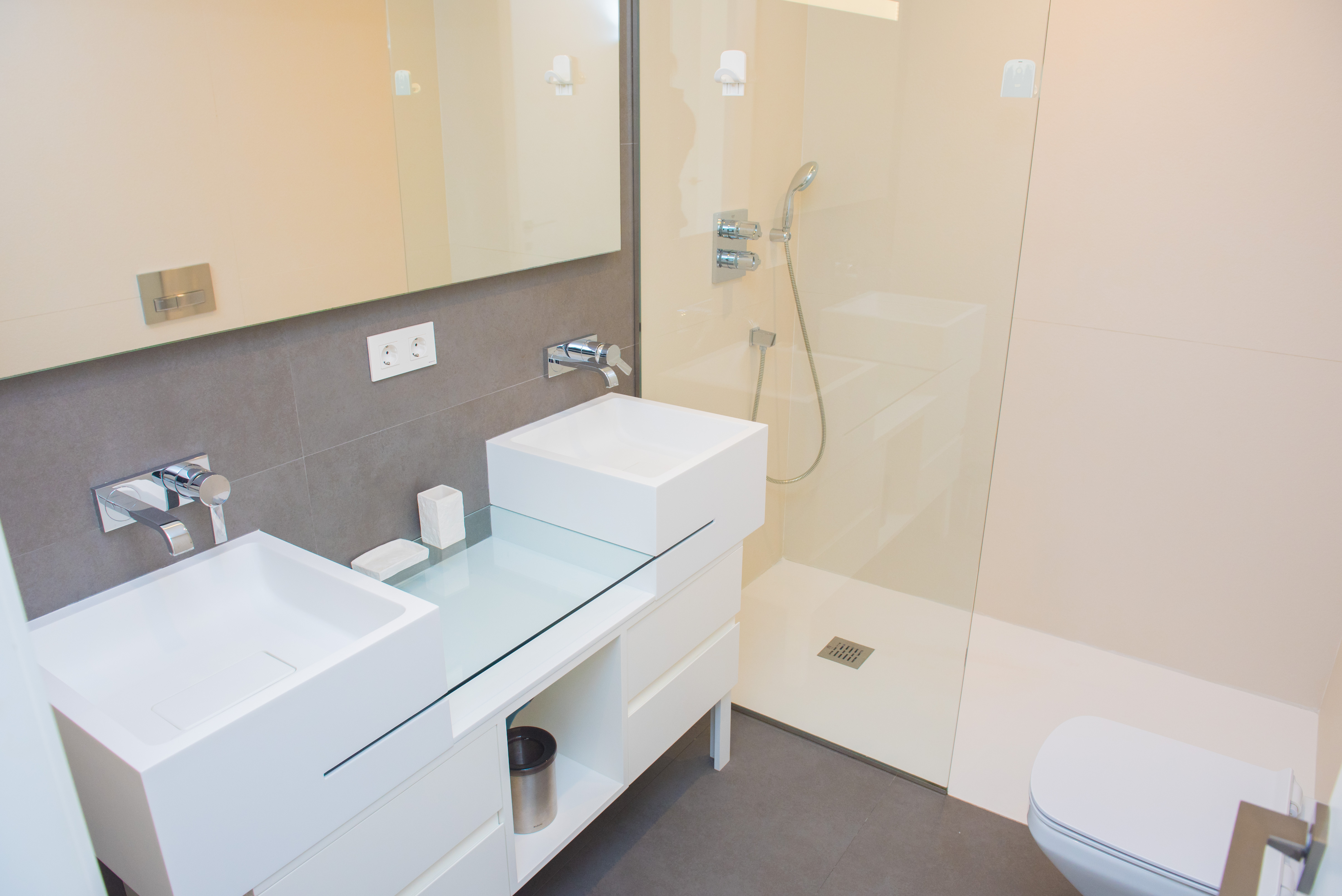 Baño moderno con lavabo doble de diseño minimalista, grifería empotrada cromada y una amplia ducha a ras de suelo con mampara de cristal fija.