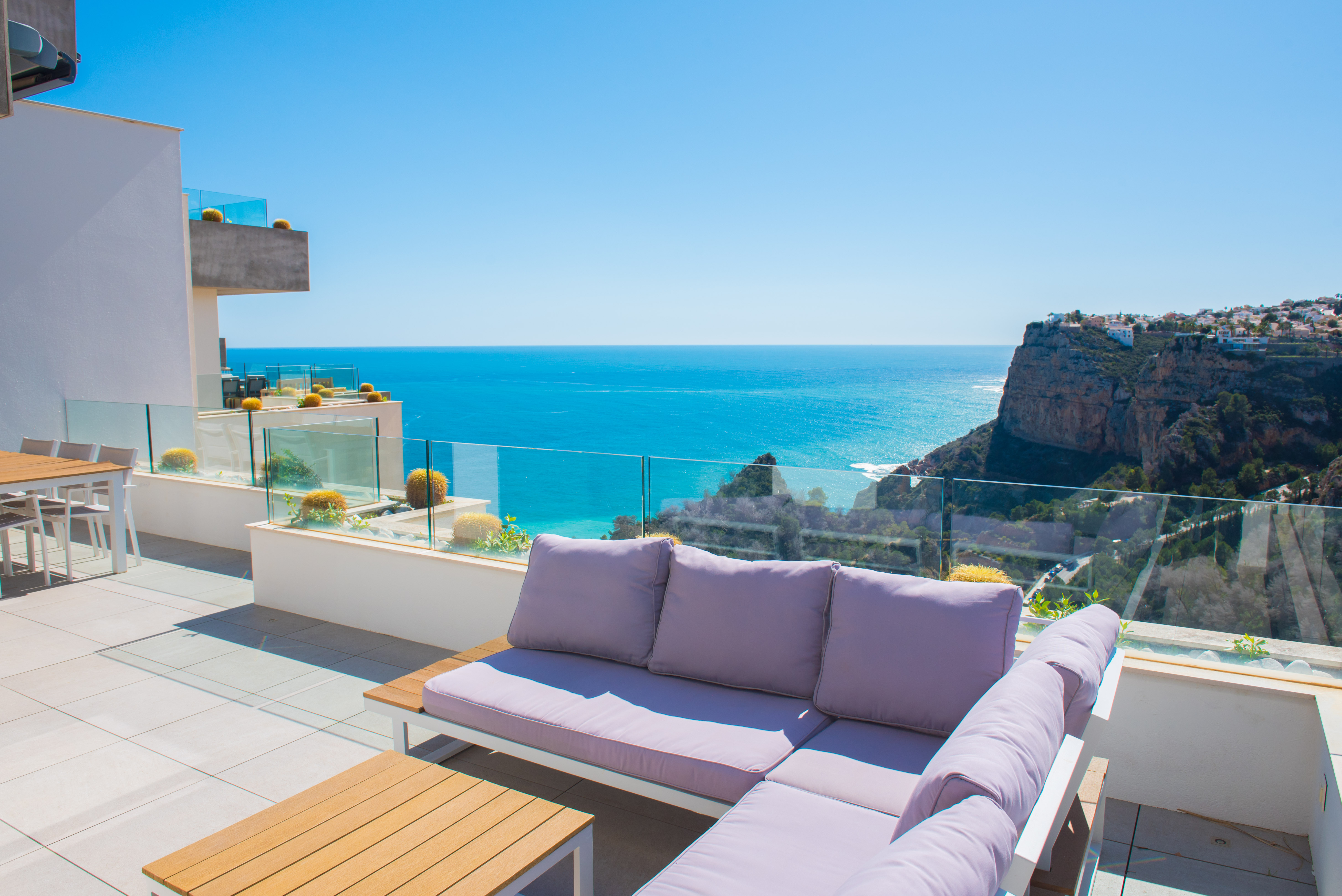 Terraza privada con mobiliario de exterior, barandillas de cristal y vistas panorámicas al mar Mediterráneo y los acantilados de Benitachell.