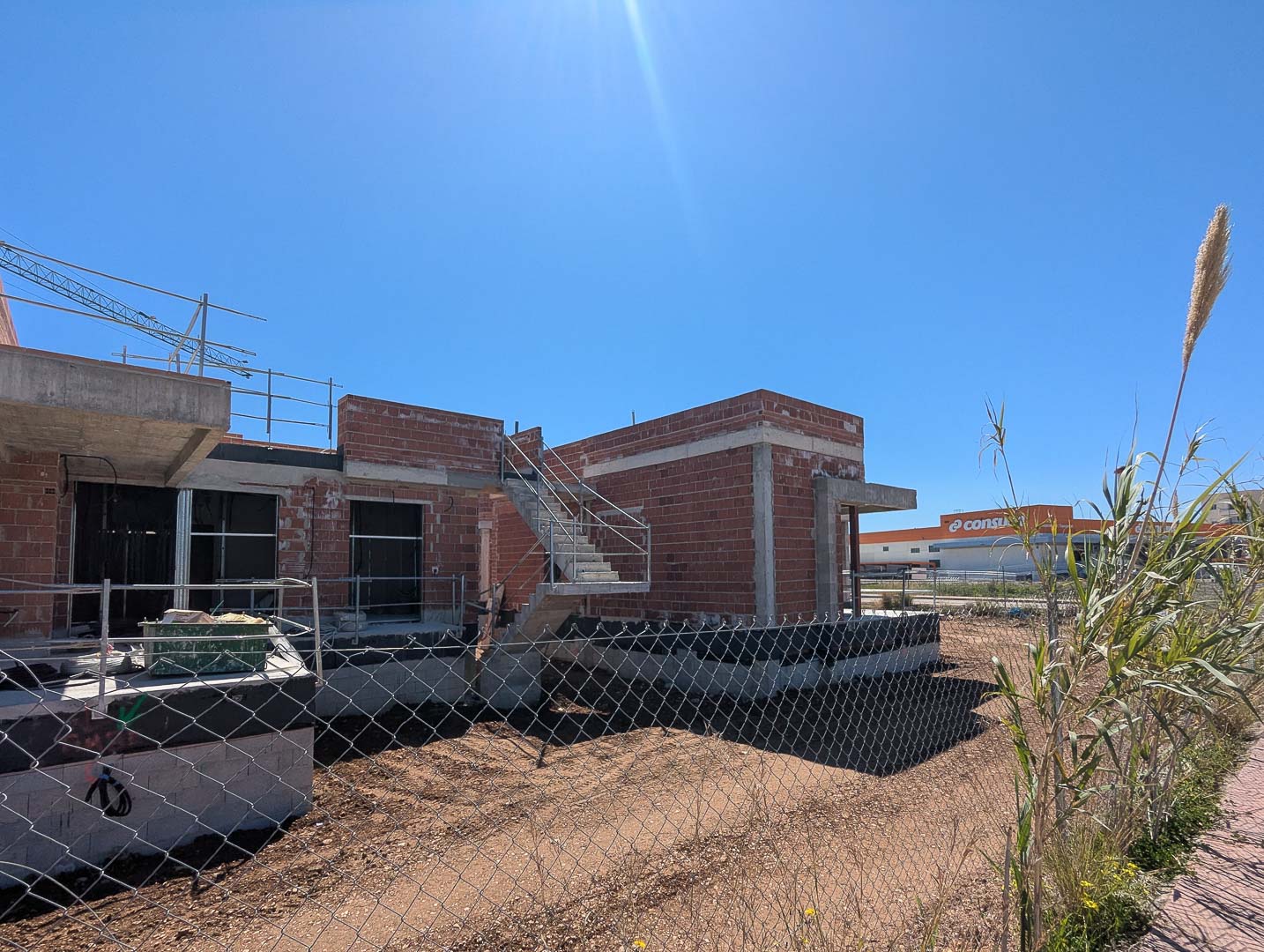 Vista exterior de la vivienda en fase de construcción, mostrando la estructura de ladrillo cerámico, escaleras de hormigón y su proximidad a servicios comerciales.