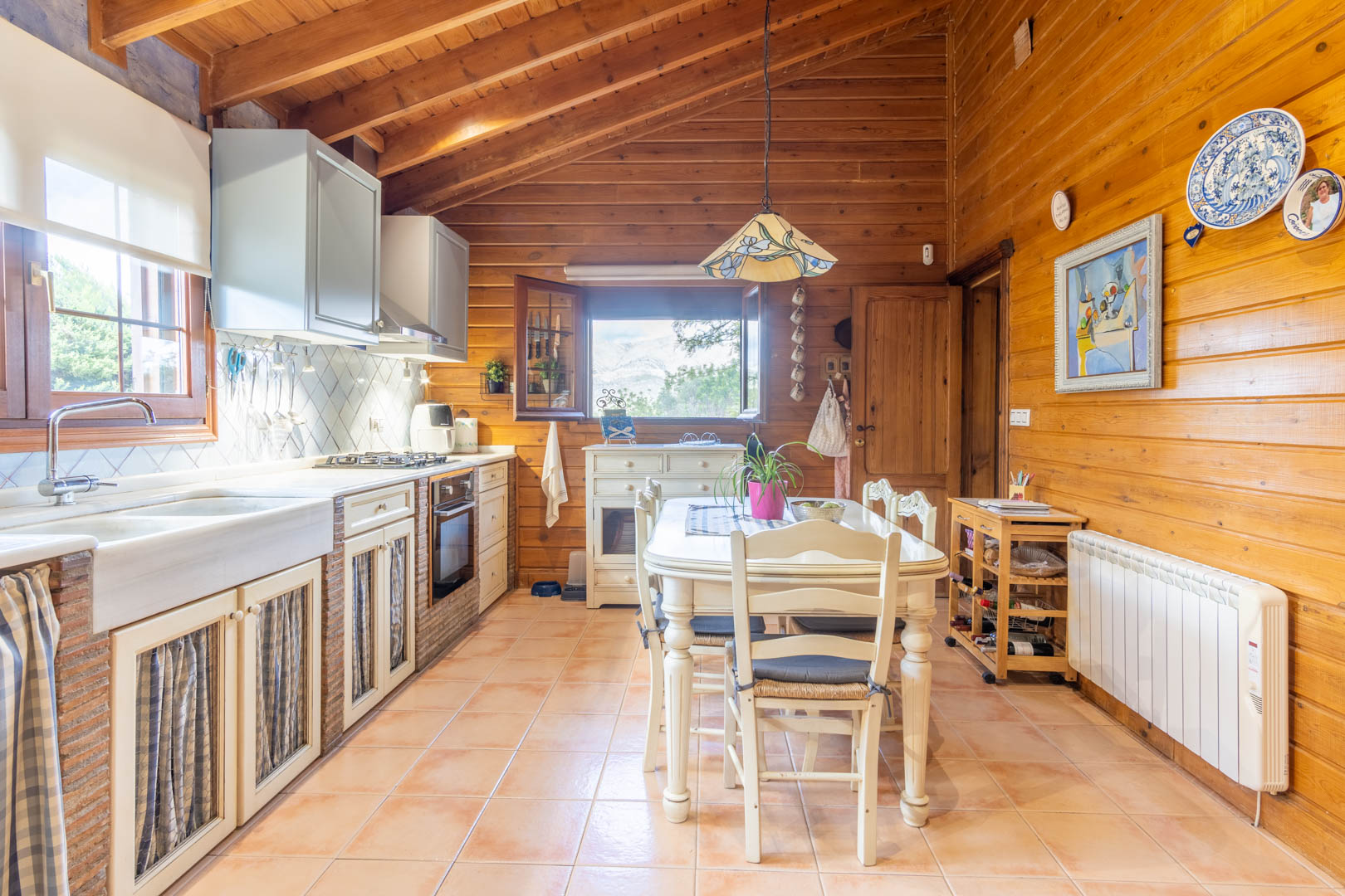 Cocina rústica con techos de pino finlandés, encimera de obra con detalles en ladrillo y zona de comedor central bajo una lámpara de estilo Tiffany.