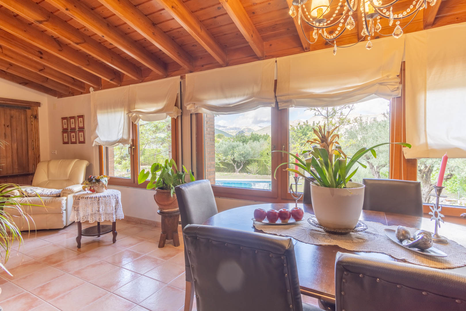 Comedor luminoso con techos de vigas de pino finlandés, suelos cerámicos y amplios ventanales que ofrecen vistas directas a la piscina y al entorno natural de Orba.
