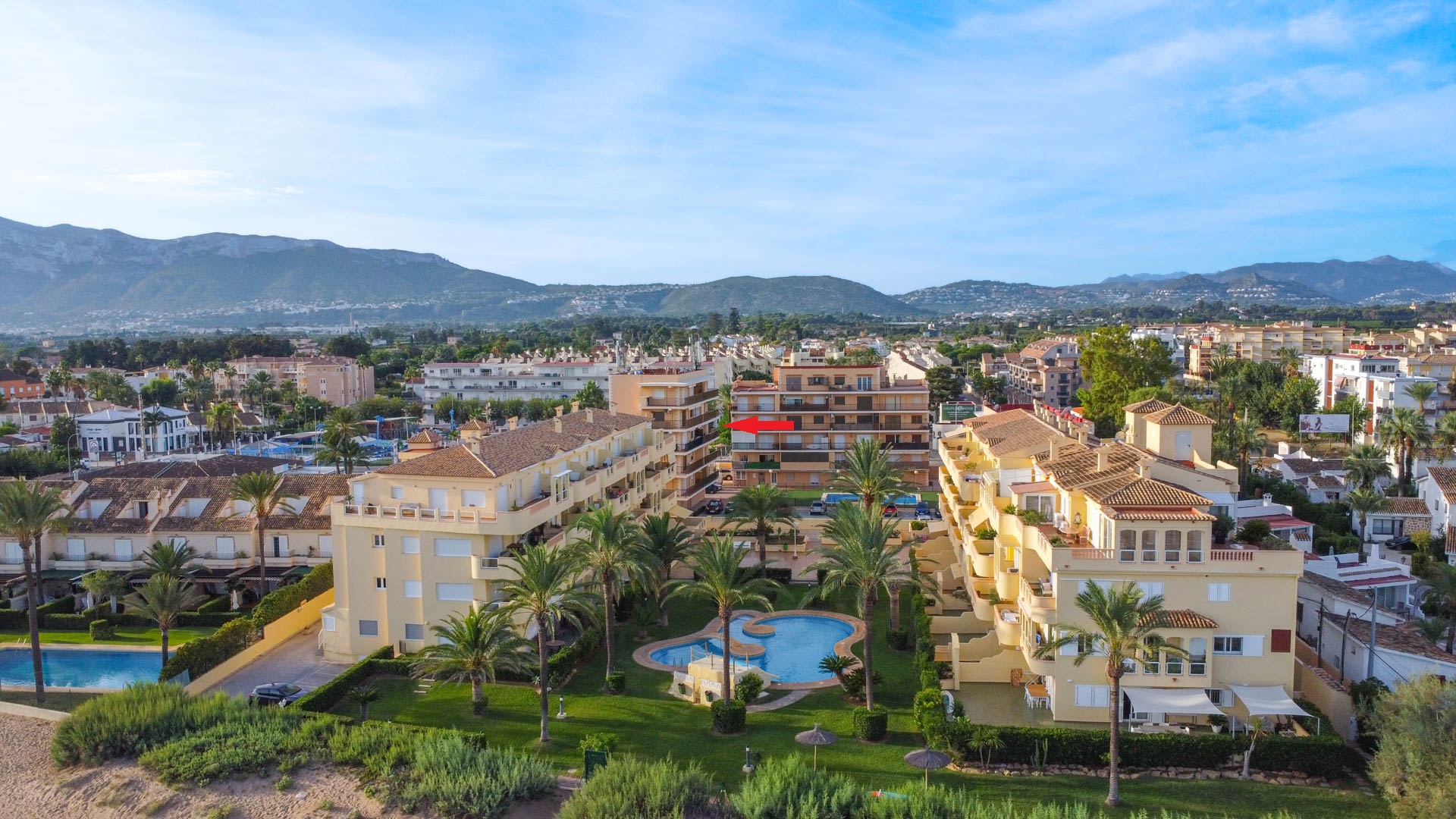Vista aérea del complejo con piscina comunitaria y jardines. Se señala la ubicación exacta de la vivienda en la tercera planta con vistas a las montañas.