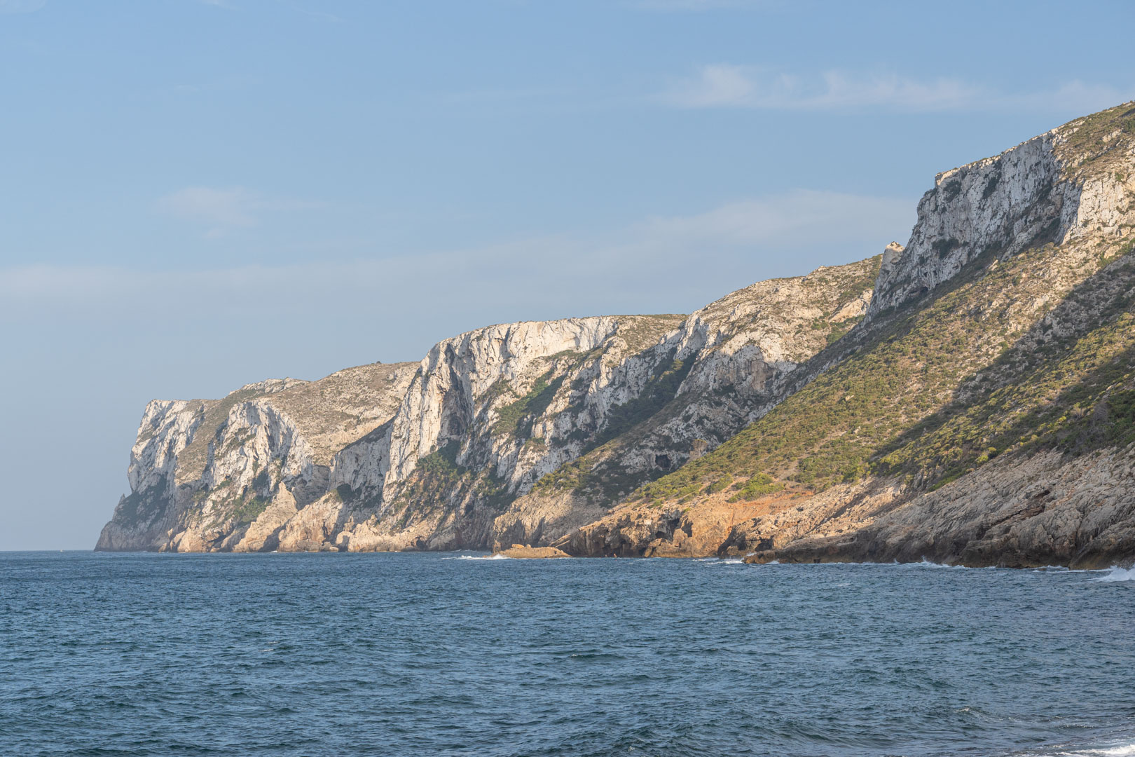 Vista panorámica de acantilados de piedra caliza sobre el mar Mediterráneo, con formaciones rocosas naturales y vegetación costera bajo un cielo despejado.