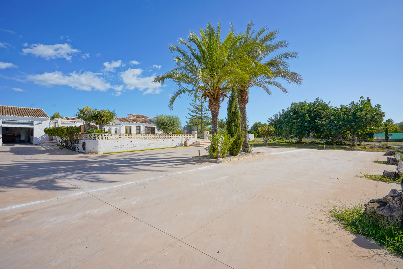 Amplio camino de entrada pavimentado con palmeras centrales, que ofrece acceso directo al garaje y a la villa blanca de estilo mediterráneo.