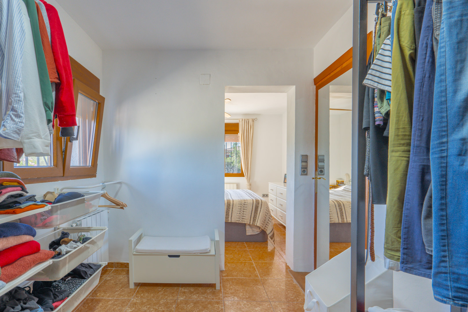 Vestidor funcional con estanterías abiertas, cajones de rejilla y zona de colgado, conectado directamente al dormitorio principal con suelos de gres cerámico.