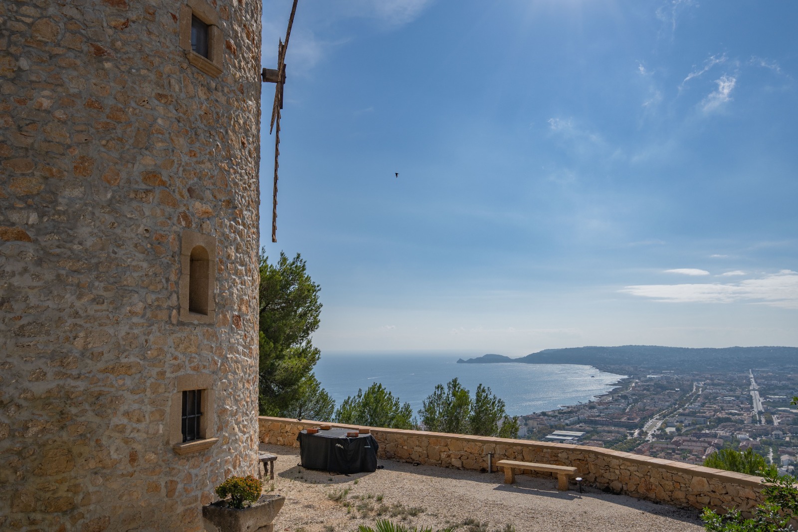 Vista panorámica desde la torre de piedra hacia la bahía de Jávea y el mar Mediterráneo, con una terraza de grava y muro perimetral de piedra natural.