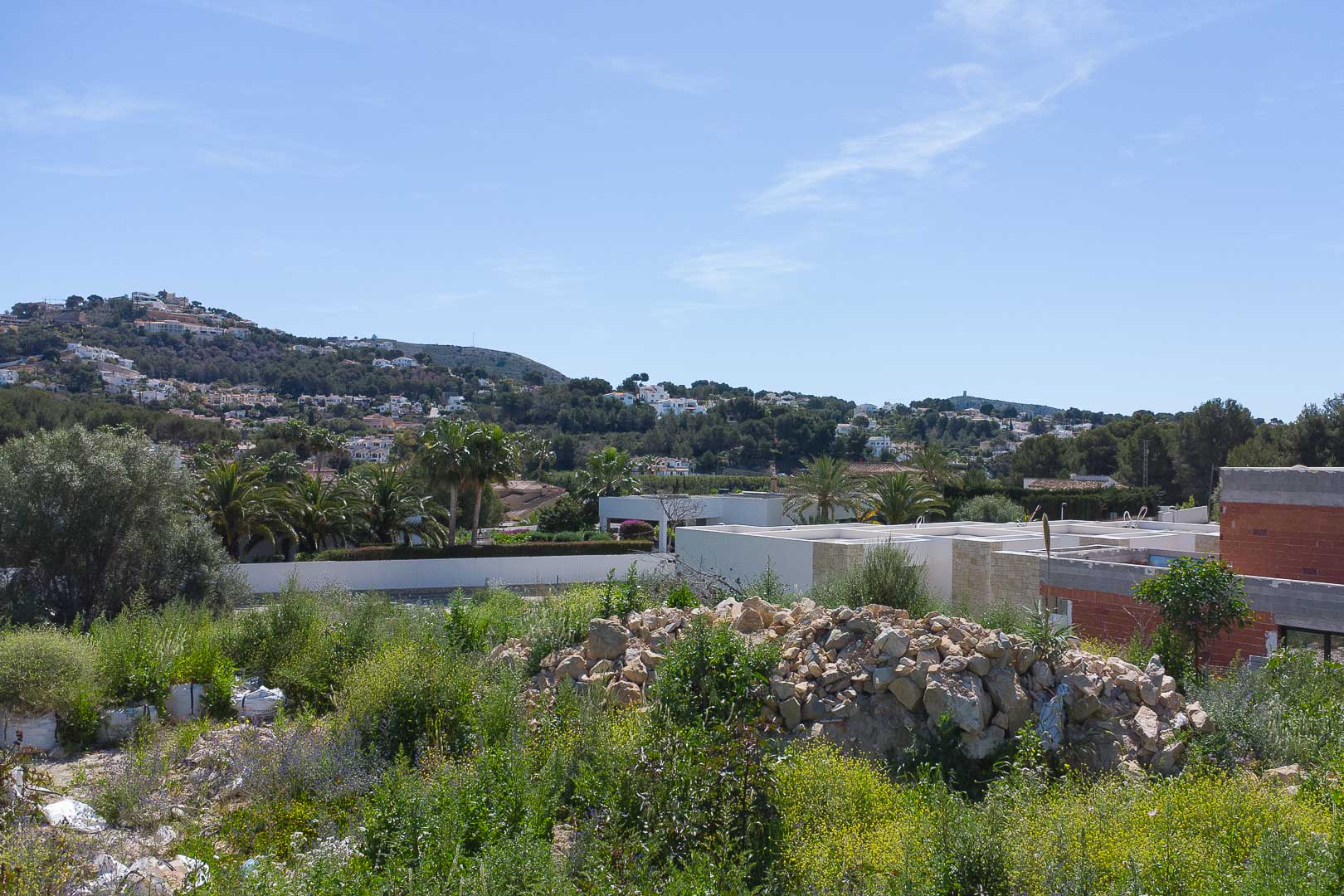 Vista panorámica desde la parcela elevada hacia las colinas de Moraira, mostrando el entorno natural y las villas circundantes bajo un cielo despejado.