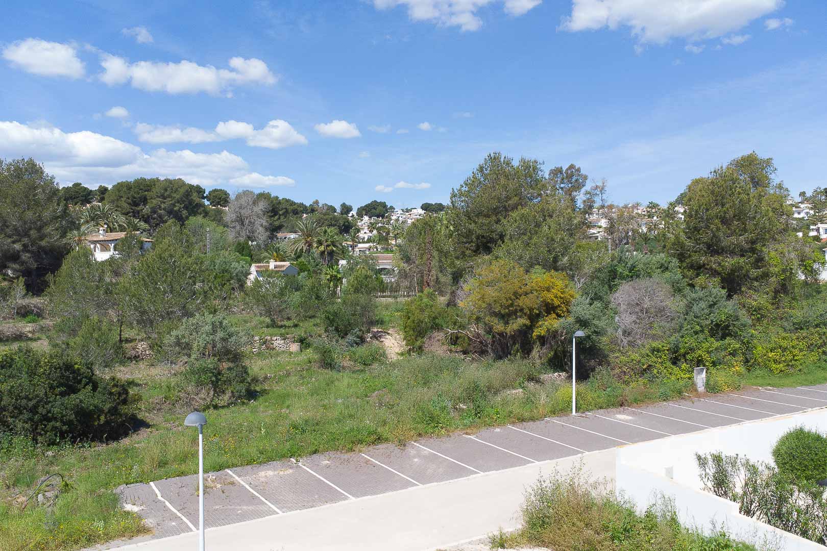 Vistas panorámicas desde la propiedad hacia el entorno natural de Moraira, mostrando la vegetación mediterránea y una zona de aparcamiento exterior bajo un cielo despejado.