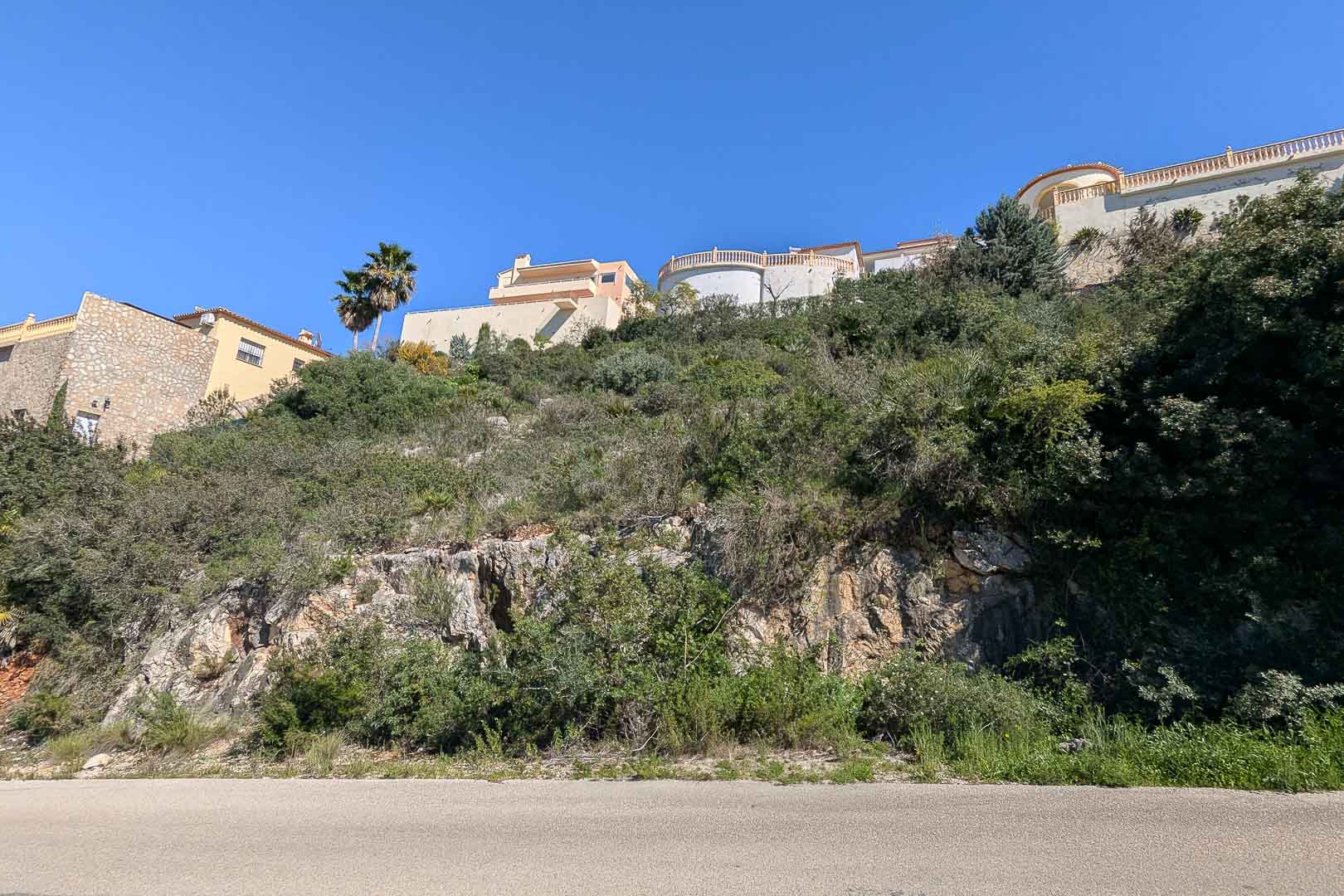 Vista exterior de una villa en construcción en Pedreguer, Costa Blanca, rodeada de vegetación mediterránea y rocas naturales.